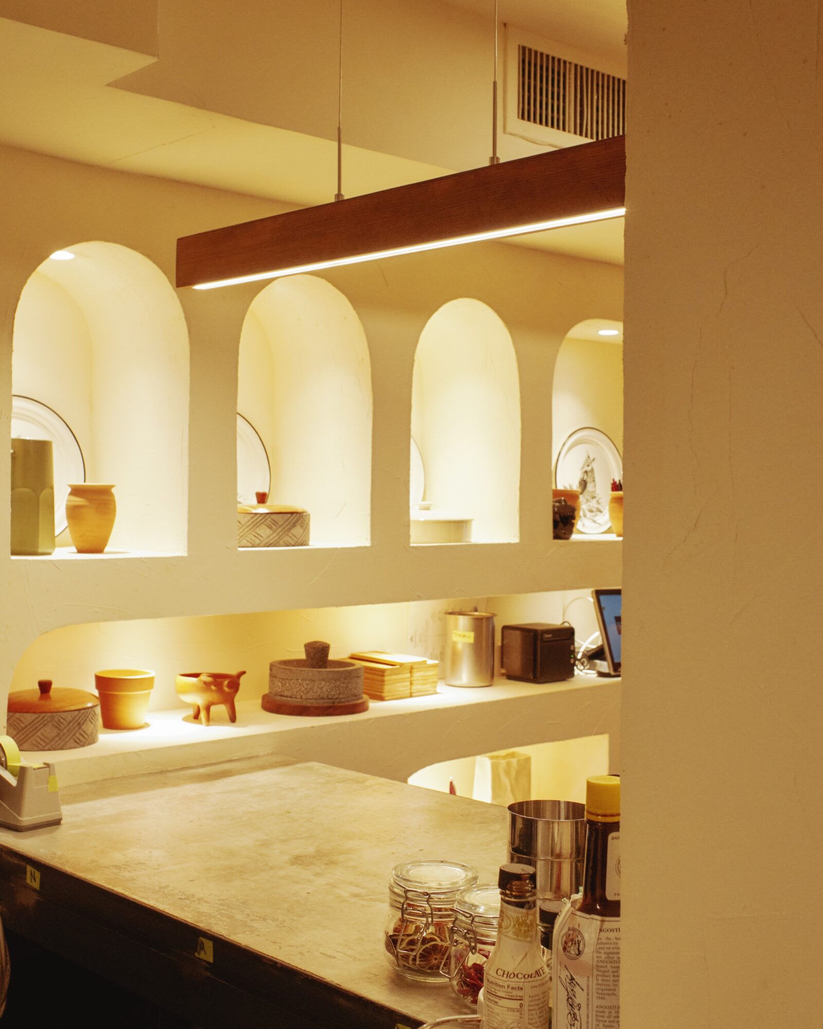 Interior view of a room with arched wall niches displaying decorative items, illuminated by warm lighting, with a countertop in the foreground.