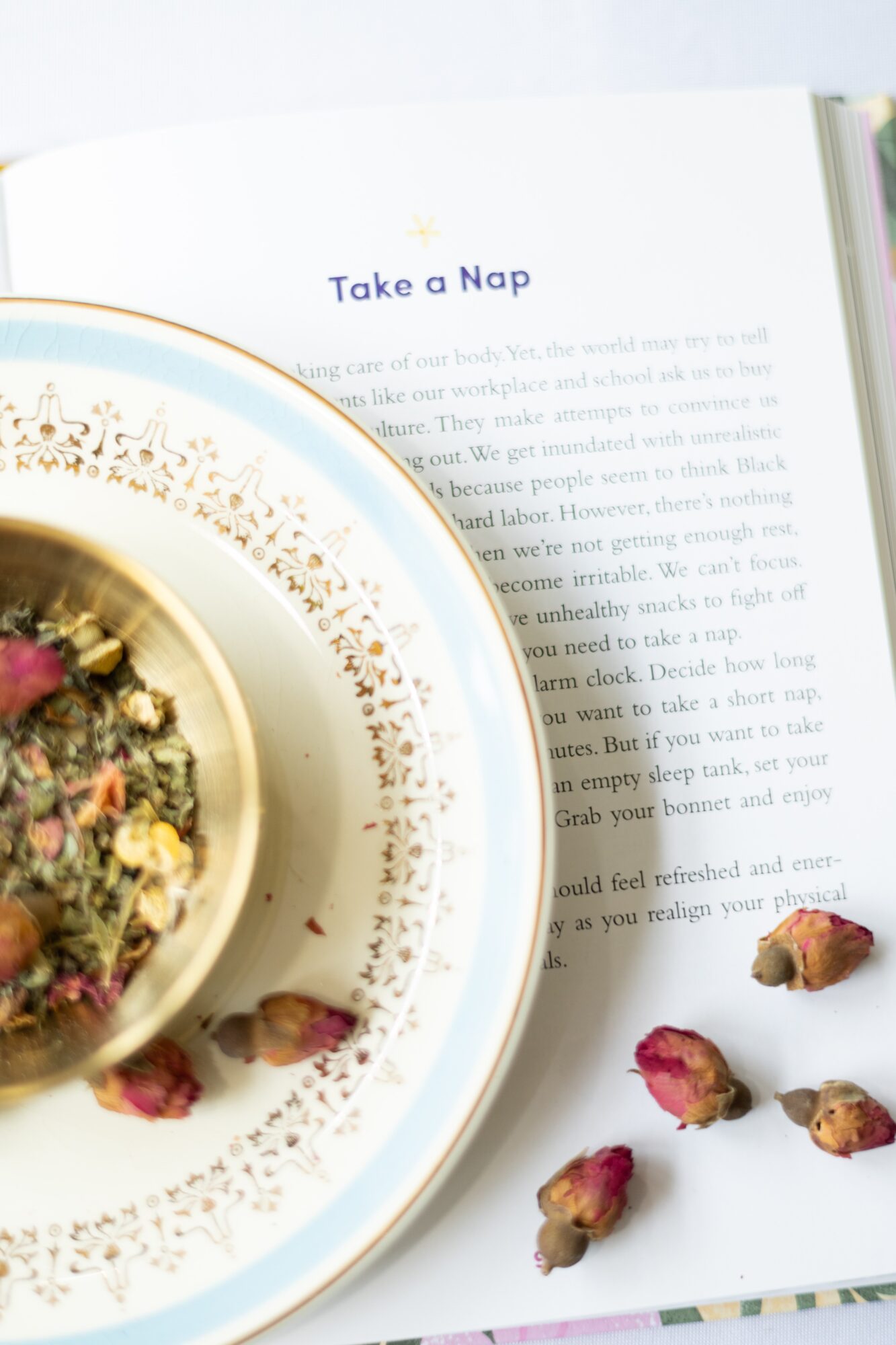 Open book with a plate of herbal tea and rosebuds on a table, text visible on the page.