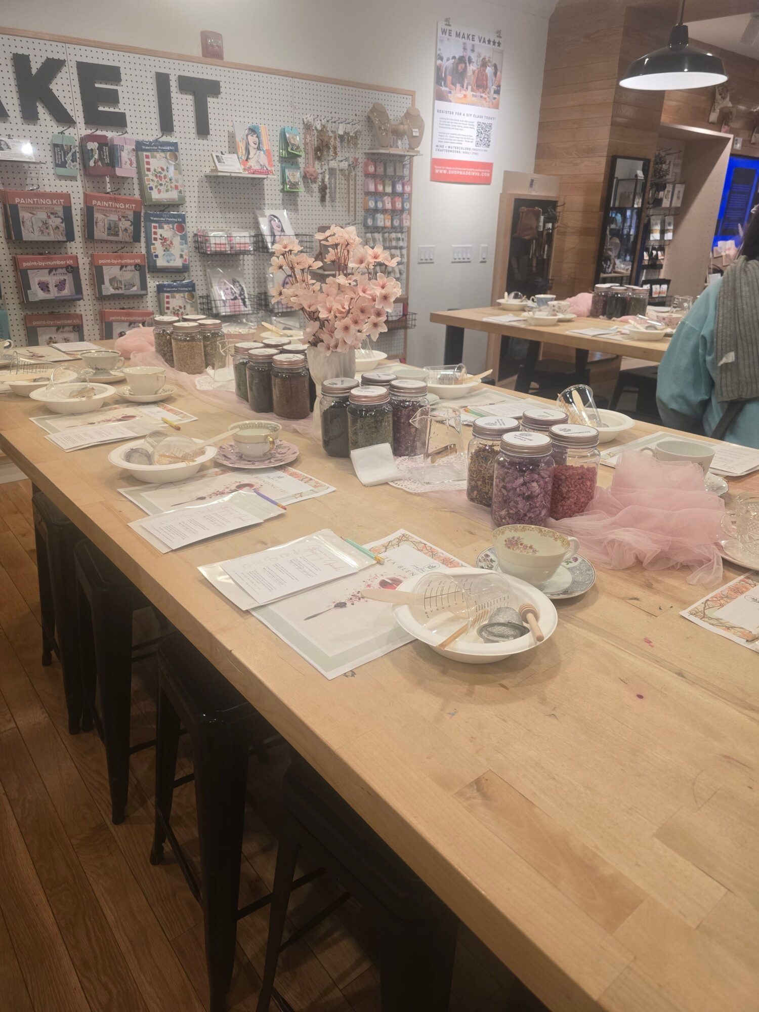 Display of various baked goods and desserts on a wooden table in a bakery or cafe, with a menu and decorative flowers in the background.