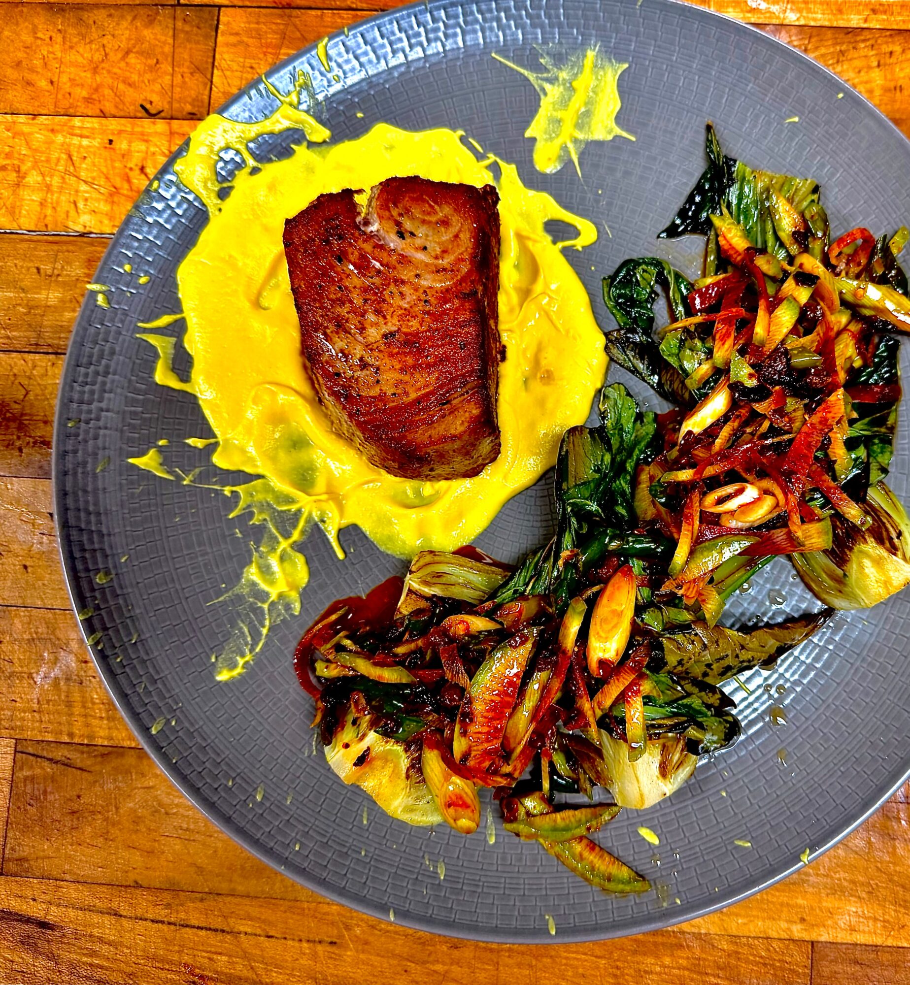Steak on yellow mashed potatoes with sautéed vegetables on a blue plate, wooden table background.