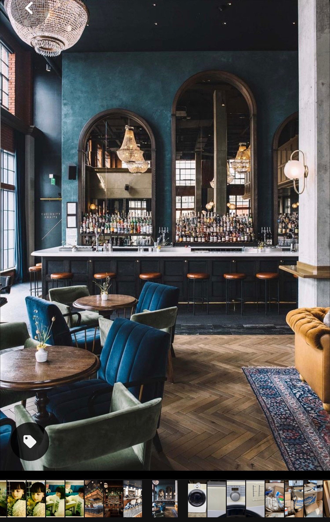 Interior of a bar with blue walls, arched mirrors, a bar counter, and seating including blue and yellow chairs, with a patterned rug.