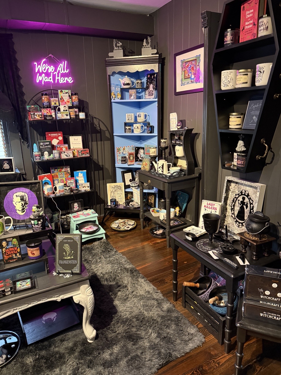 Interior of a store with shelves displaying books, candles, and decorative items, a black table with accessories, and a gray rug.