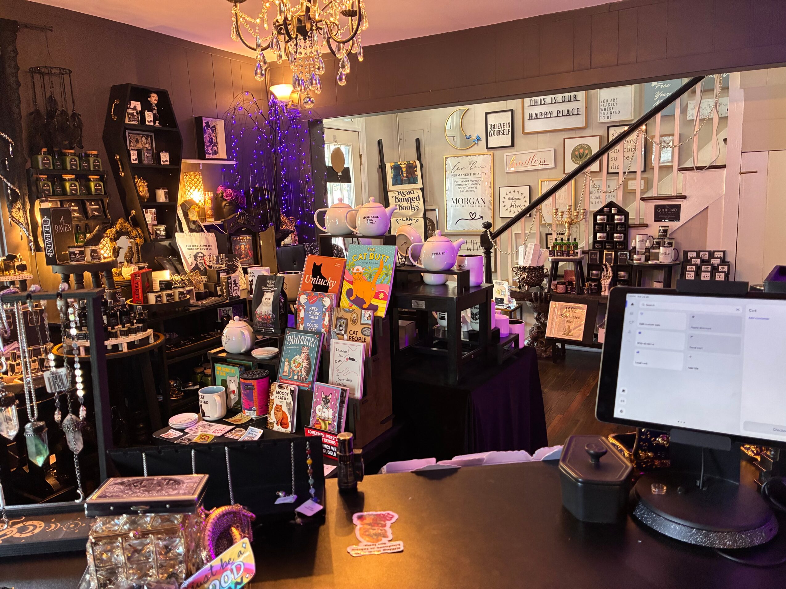 Interior of a boutique store with shelves, displays, and a computer on a desk, decorated with lights and artwork.