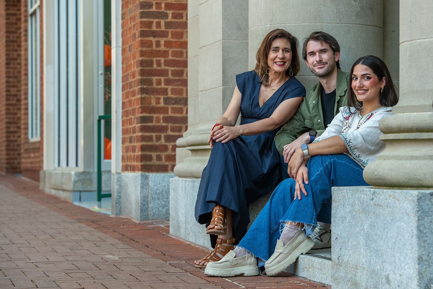Three people sitting on a stone ledge outside a building, smiling and posing for the photo.