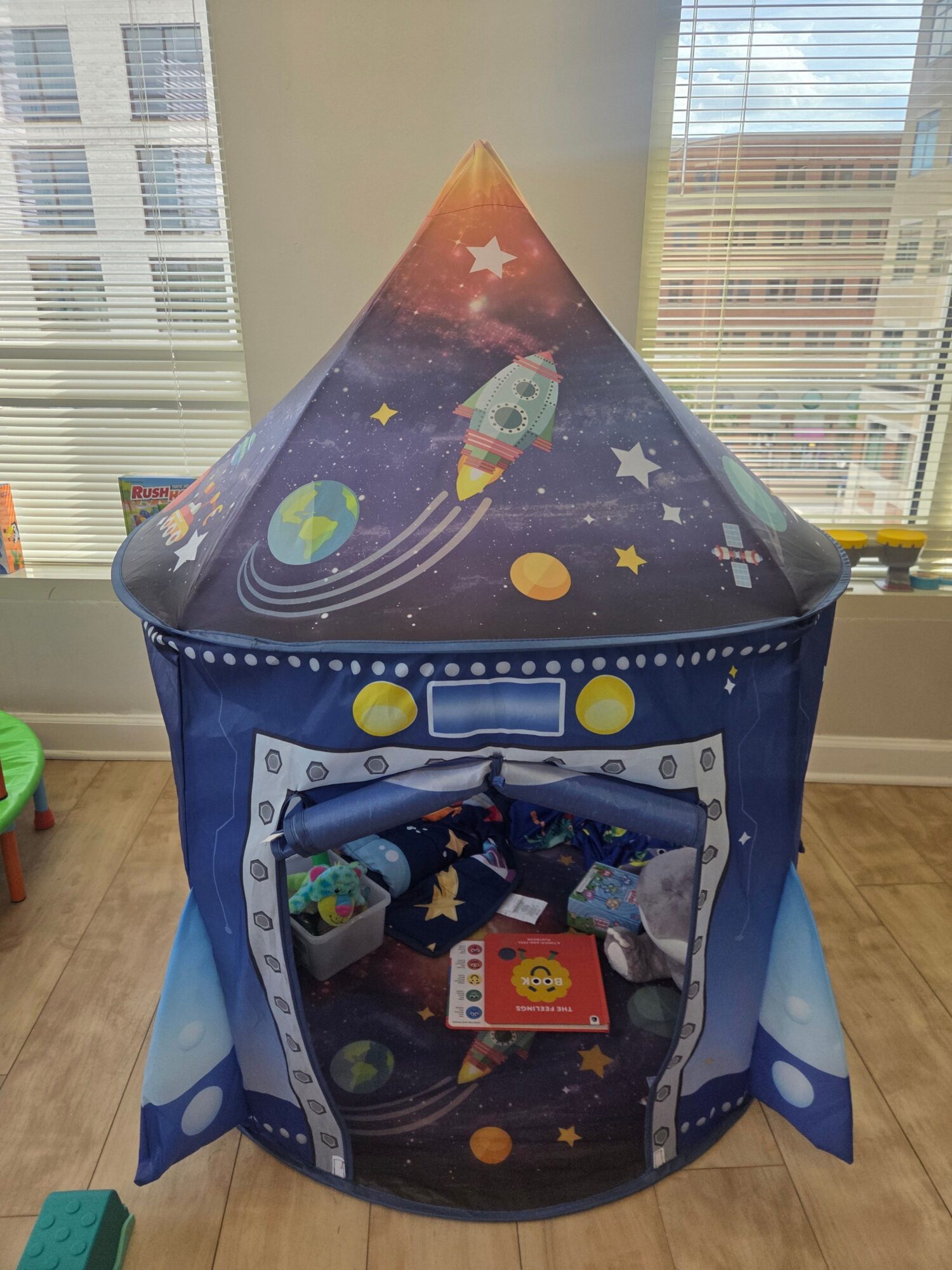 Children's play tent with space theme, featuring rockets, planets, and stars, set up indoors on wooden floor.
