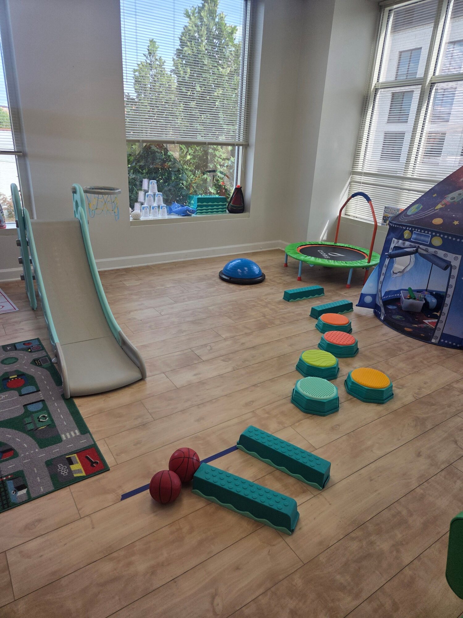 Indoor play area with toys and equipment near a window showing trees outside.