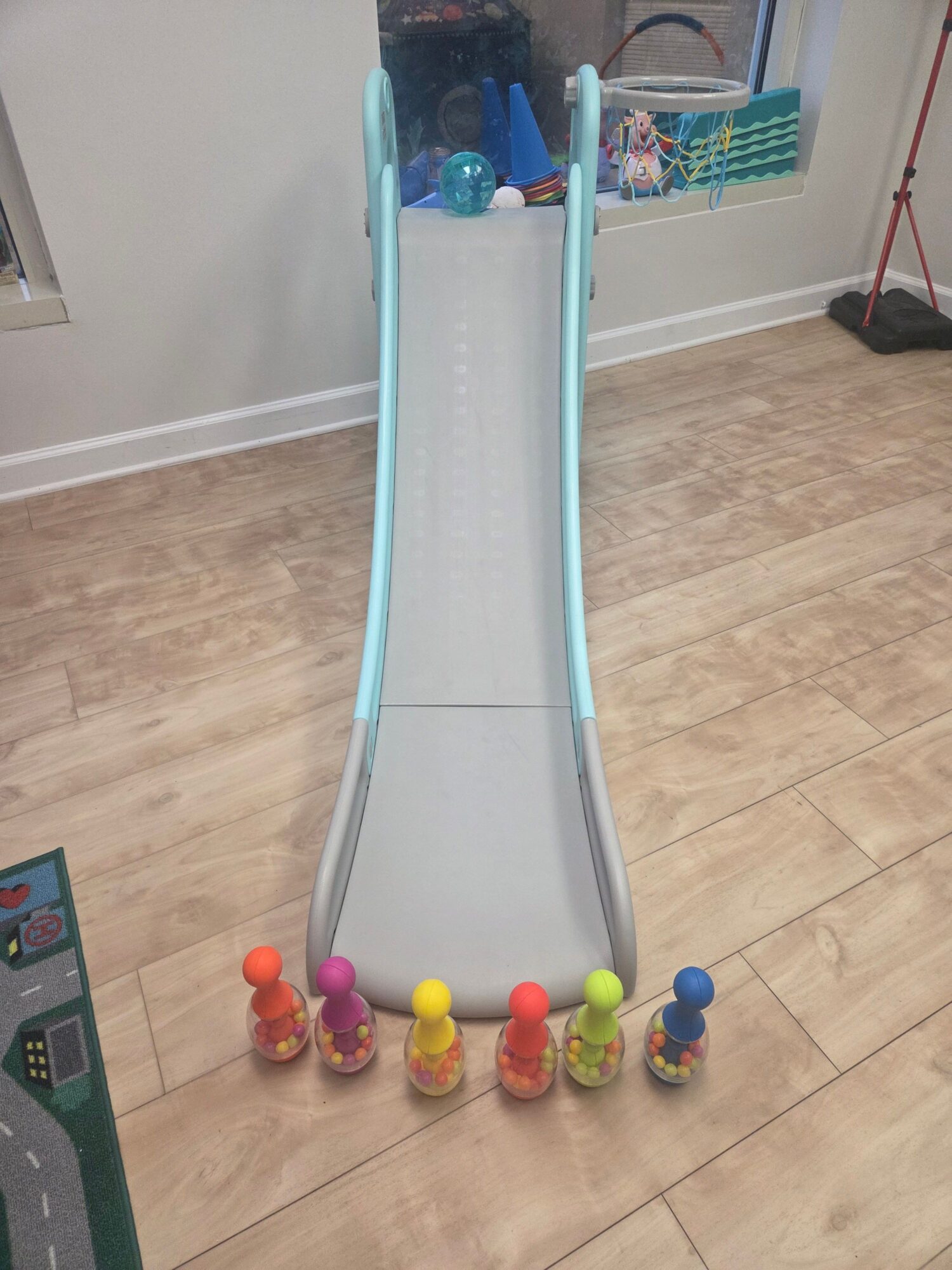Colorful toy slide with small balls at the bottom, on a wooden floor in a room.