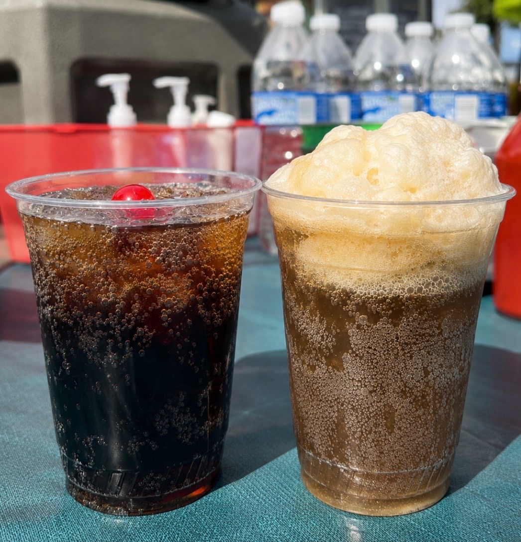 Two cups, one with a dark soda and a cherry, the other with a frothy, light-colored beverage, on a table.
