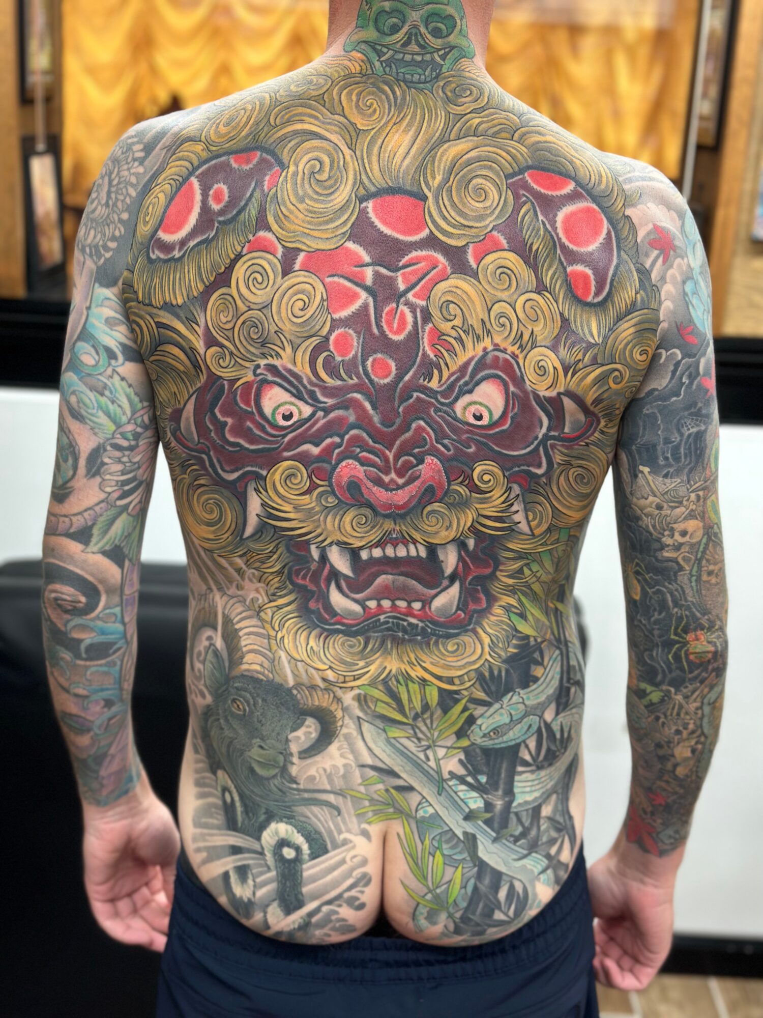 Back view of a person with a large, colorful tattoo of a fierce lion's face with intricate details and patterns.