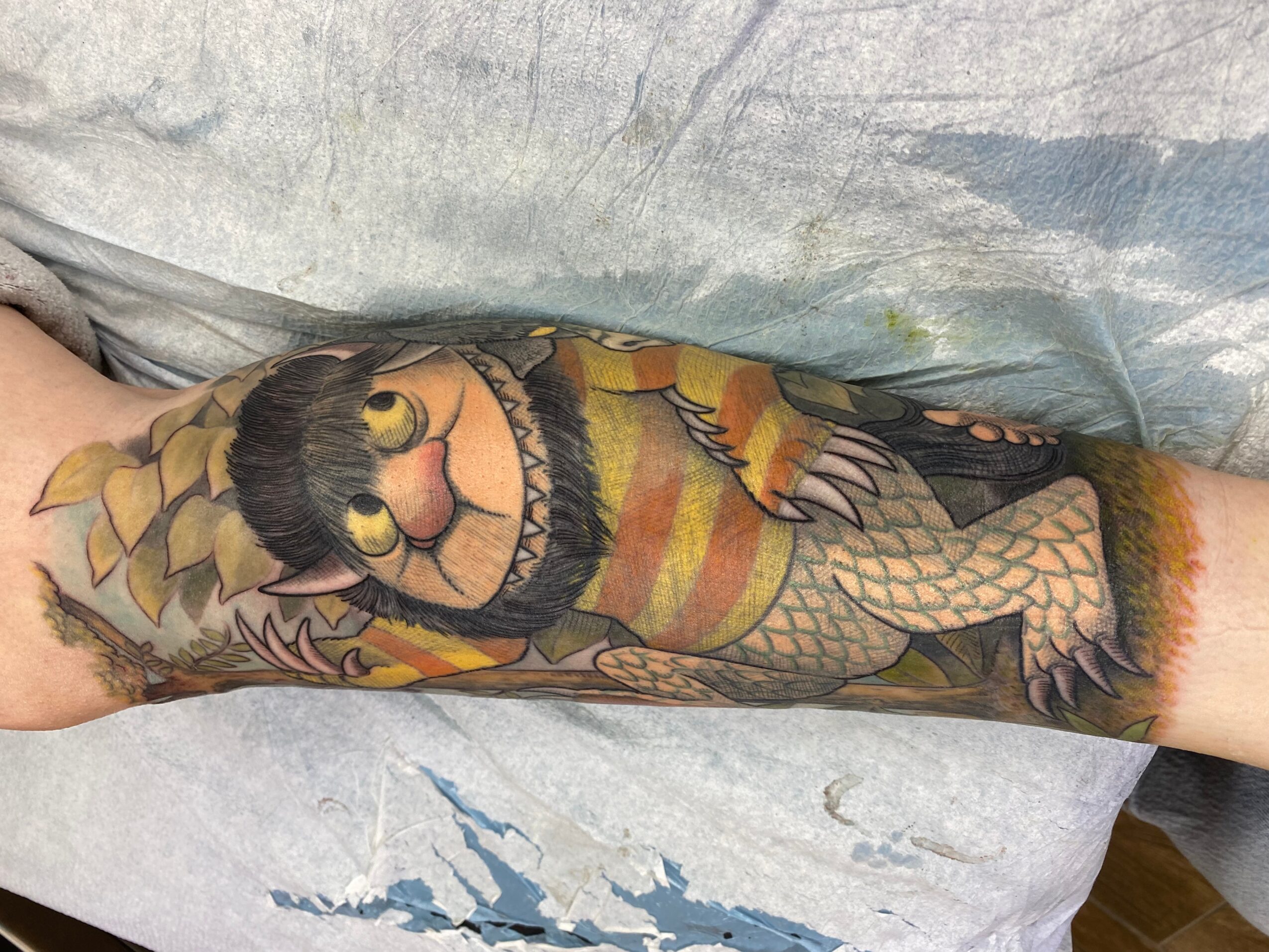 Colorful tattoo of a smiling fish with a yellow and orange body, black fins, and a friendly face on a person's arm.