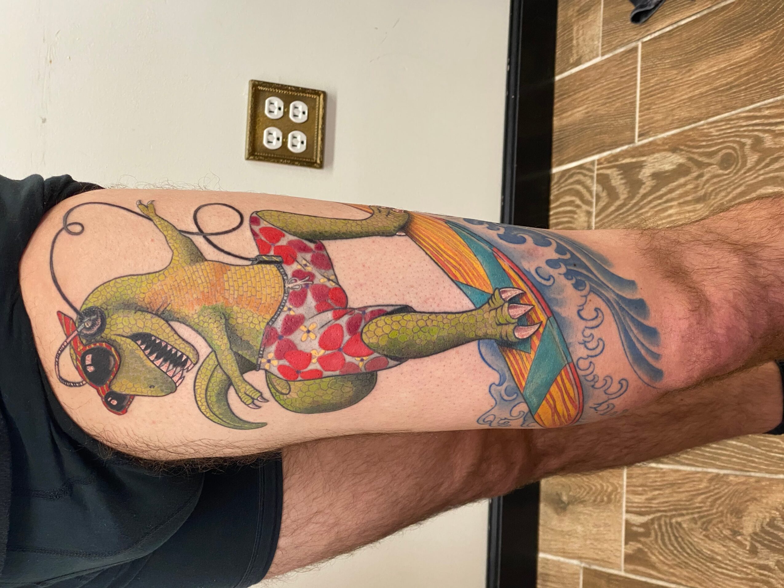 Colorful tattoo of an octopus wearing red shorts and sunglasses, with a background of waves and sky, on a person's leg.