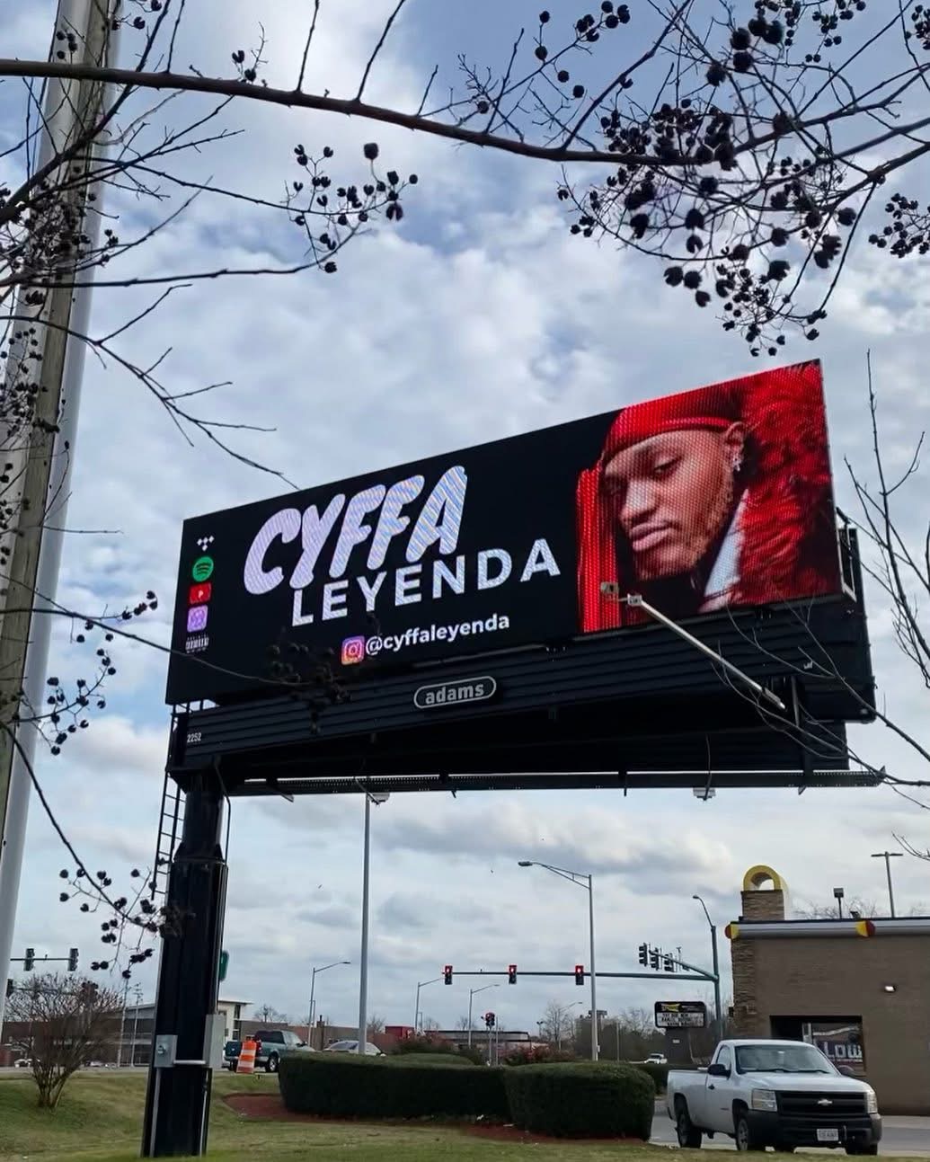 Billboard displays a woman with a red headscarf and makeup, with text 'CYFA LEYENDA' and social media handle '@cyfayleyenda'.
