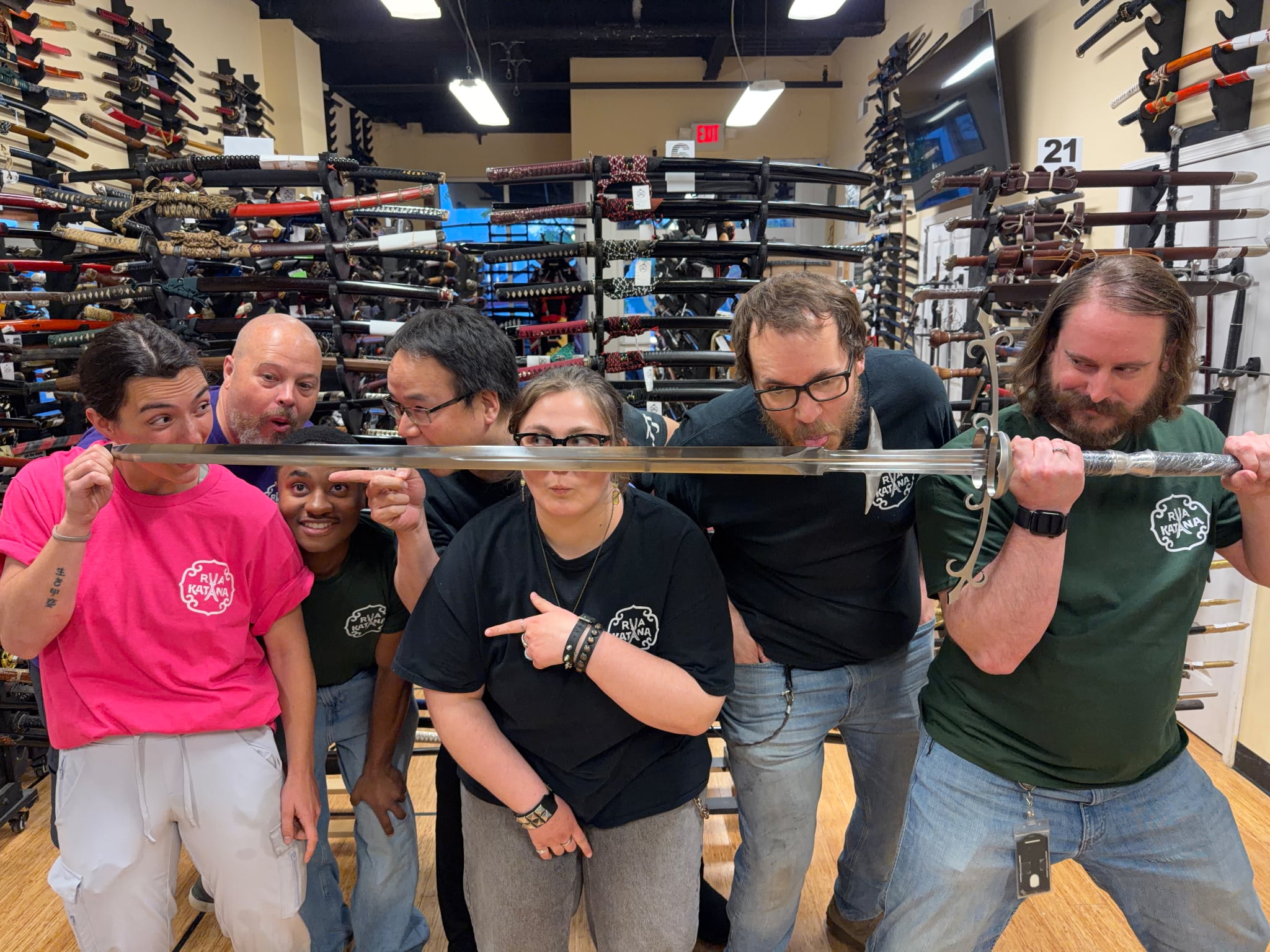 Group of six people in a store with shelves of swords behind them, some holding a long sword, smiling and posing.