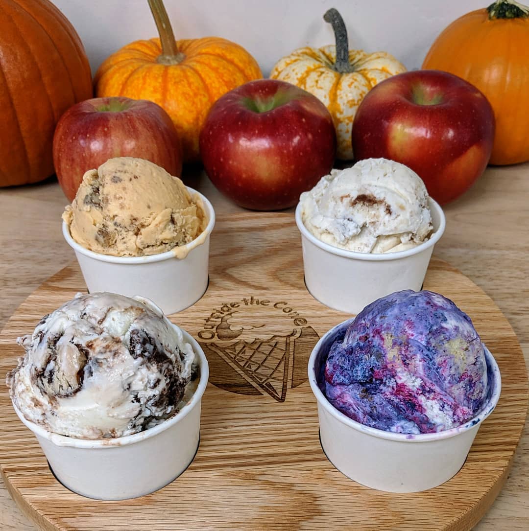 Four cups of ice cream on a wooden tray with apples and pumpkins in the background.