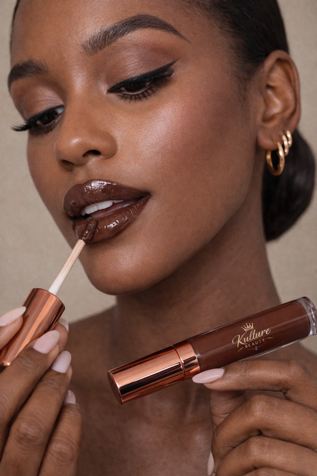 Close-up of woman applying dark lipstick with a tube in her hand, wearing gold hoop earrings, makeup, and a neutral background.