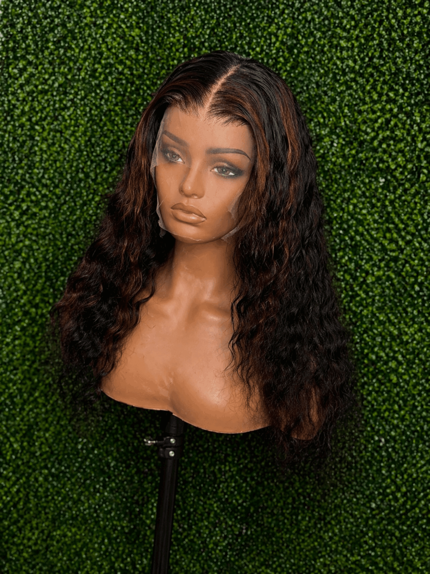Bust of a woman with long, wavy hair against a green leafy background, looking slightly to the side.