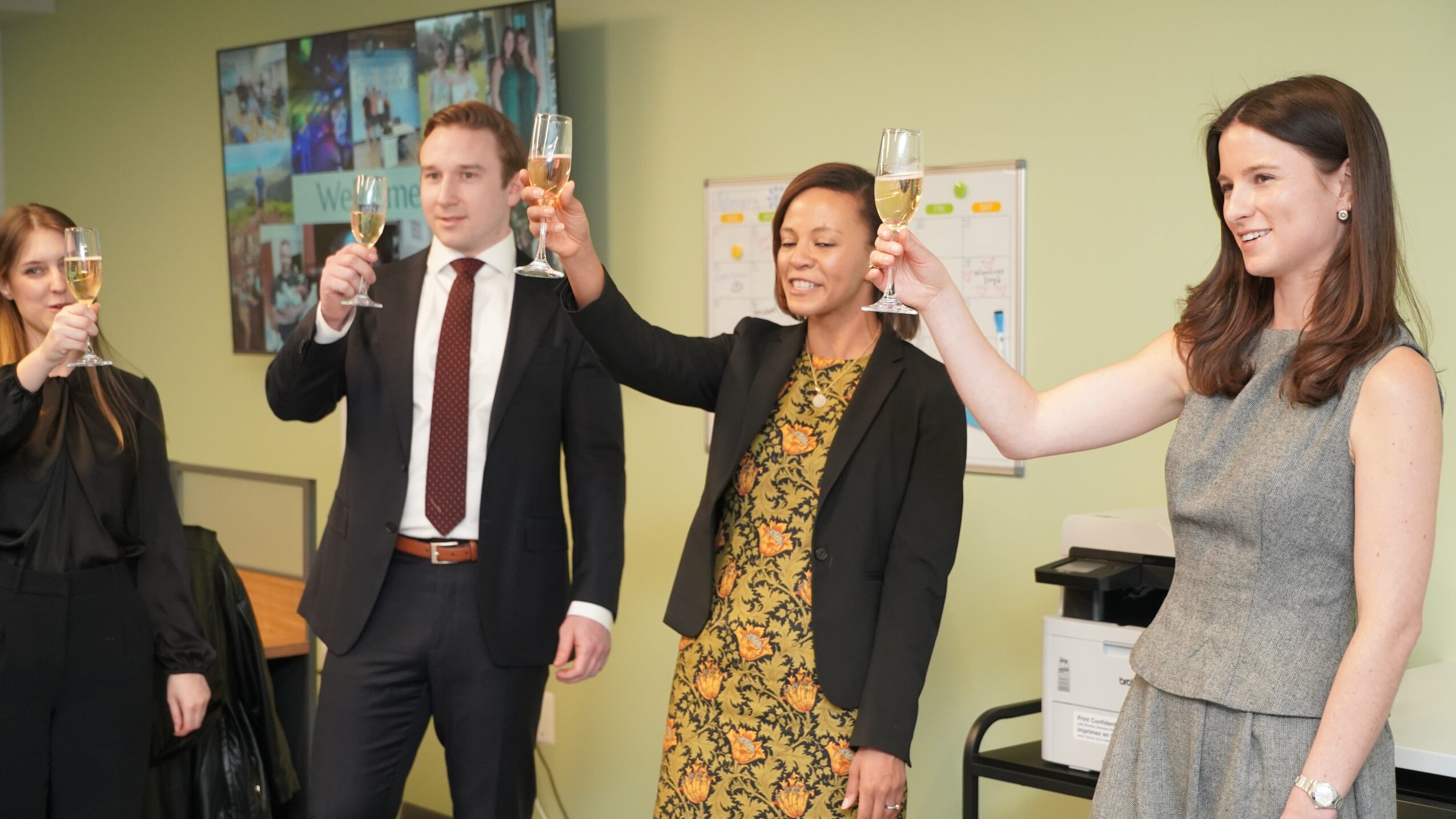Four people raising glasses in a toast at a celebration in an office setting.