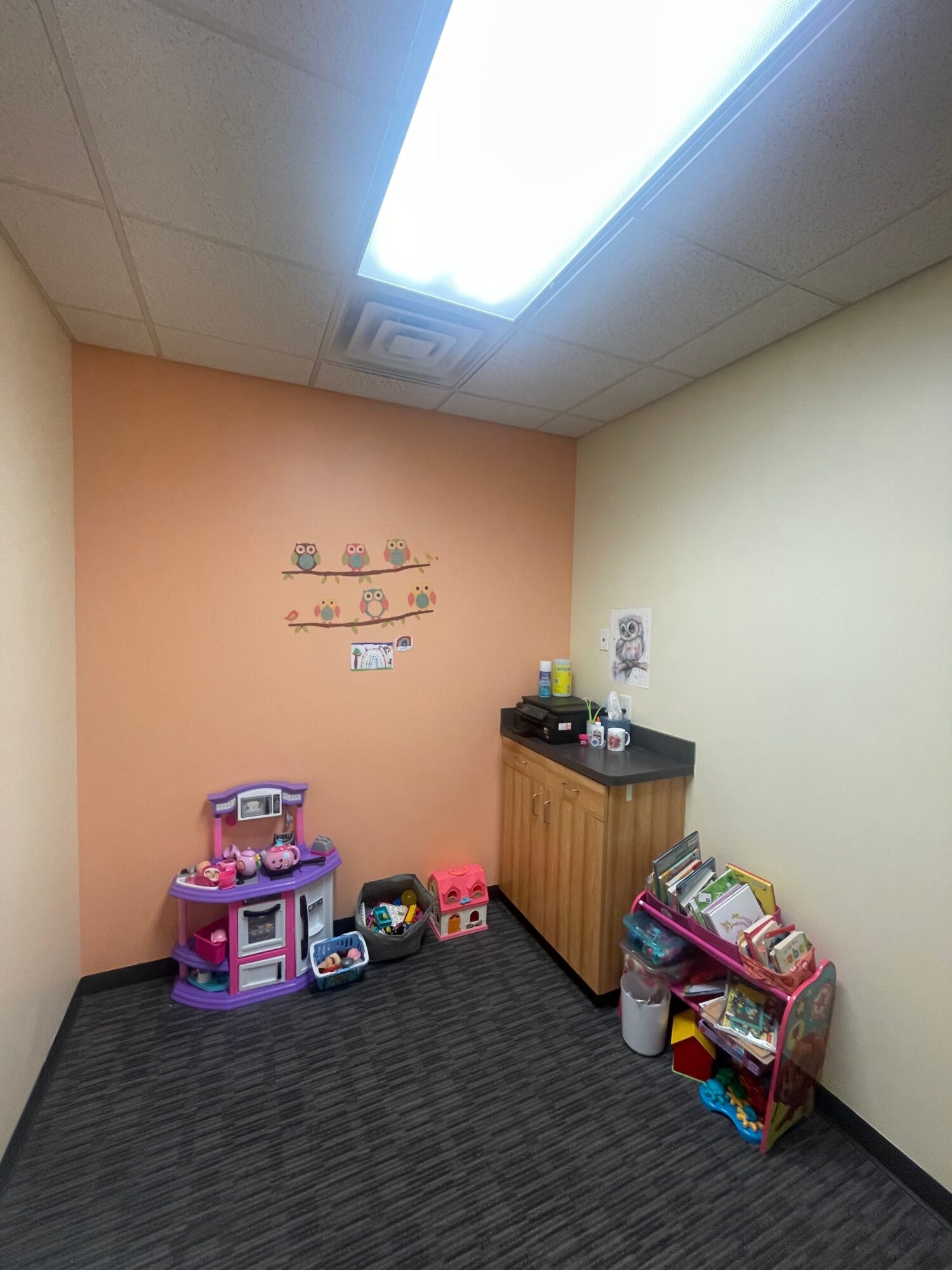 Corner of a room with a pink wall, wooden cabinet, and children's toys on the floor, with a window overhead.