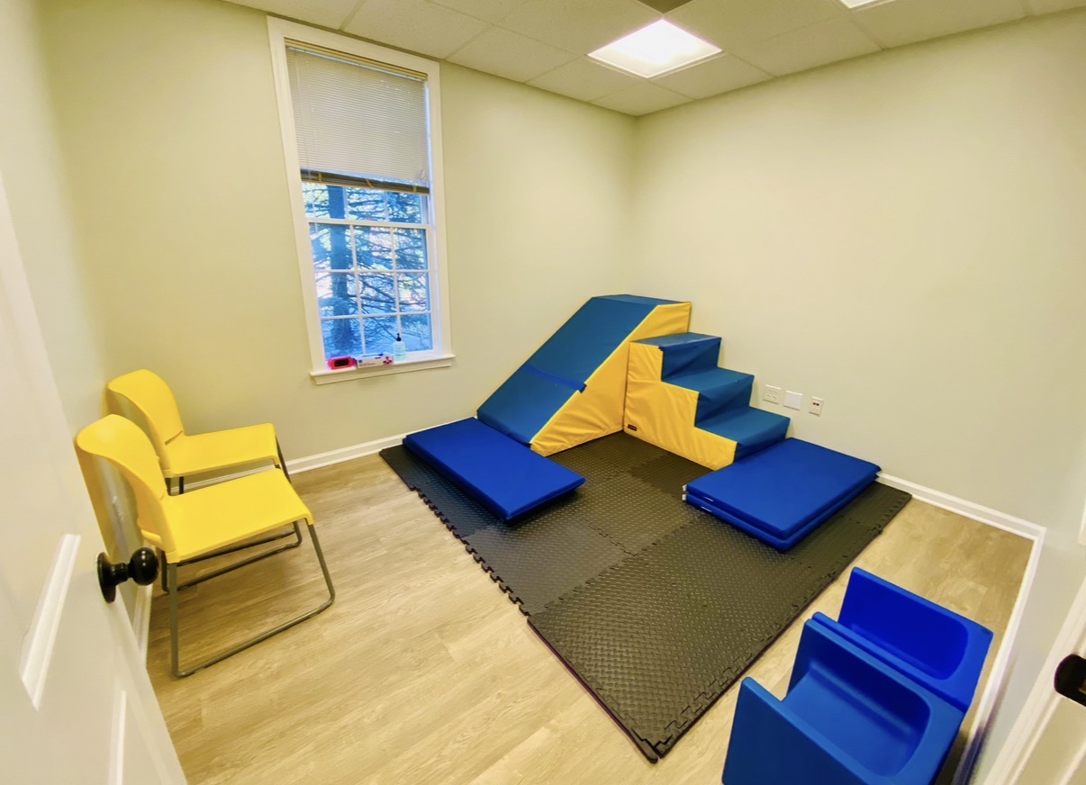 Room with yellow chair, window, and colorful foam climbing structure on black mat, blue blocks, and light-colored floor.