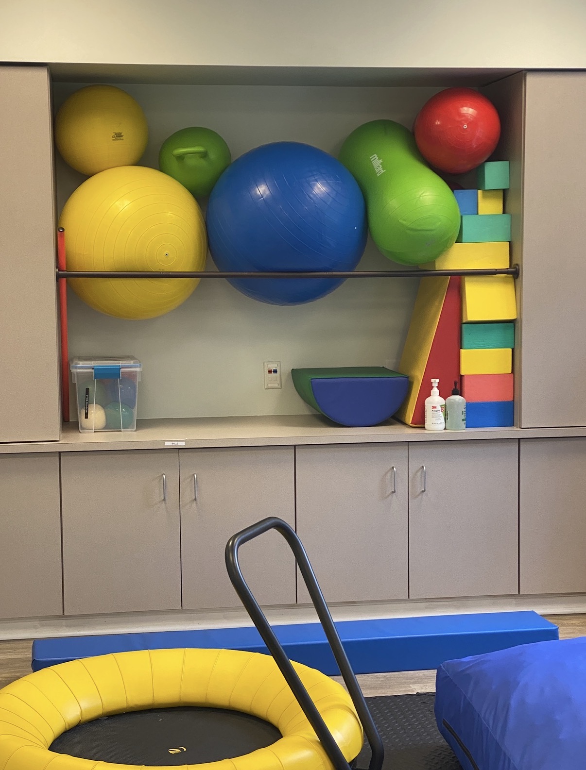 Colorful exercise balls and stacking blocks in a play area with storage cabinets and a blue mat.