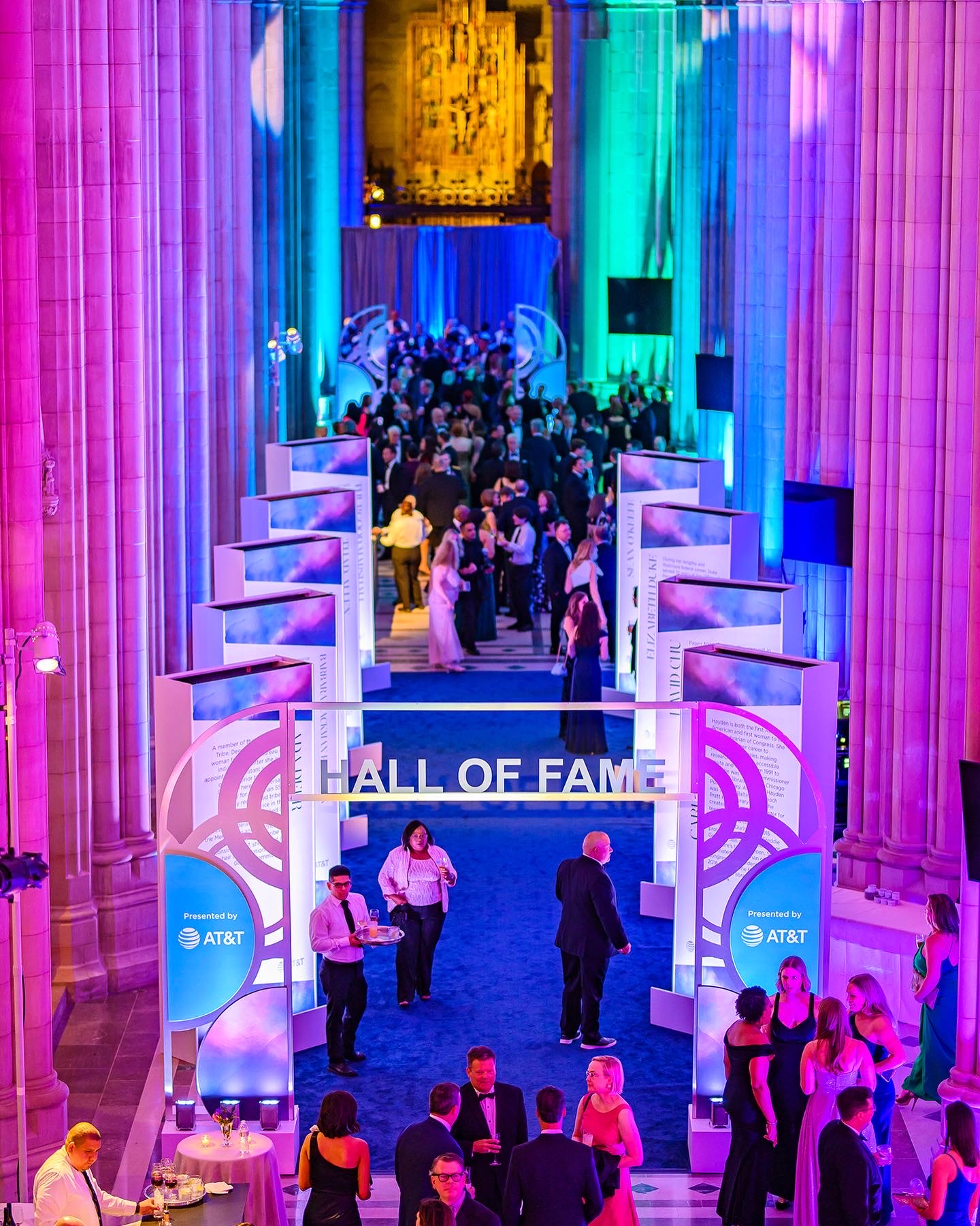 People gather at the AT&T Hall of Fame entrance with colorful lighting and large columns, celebrating an event.