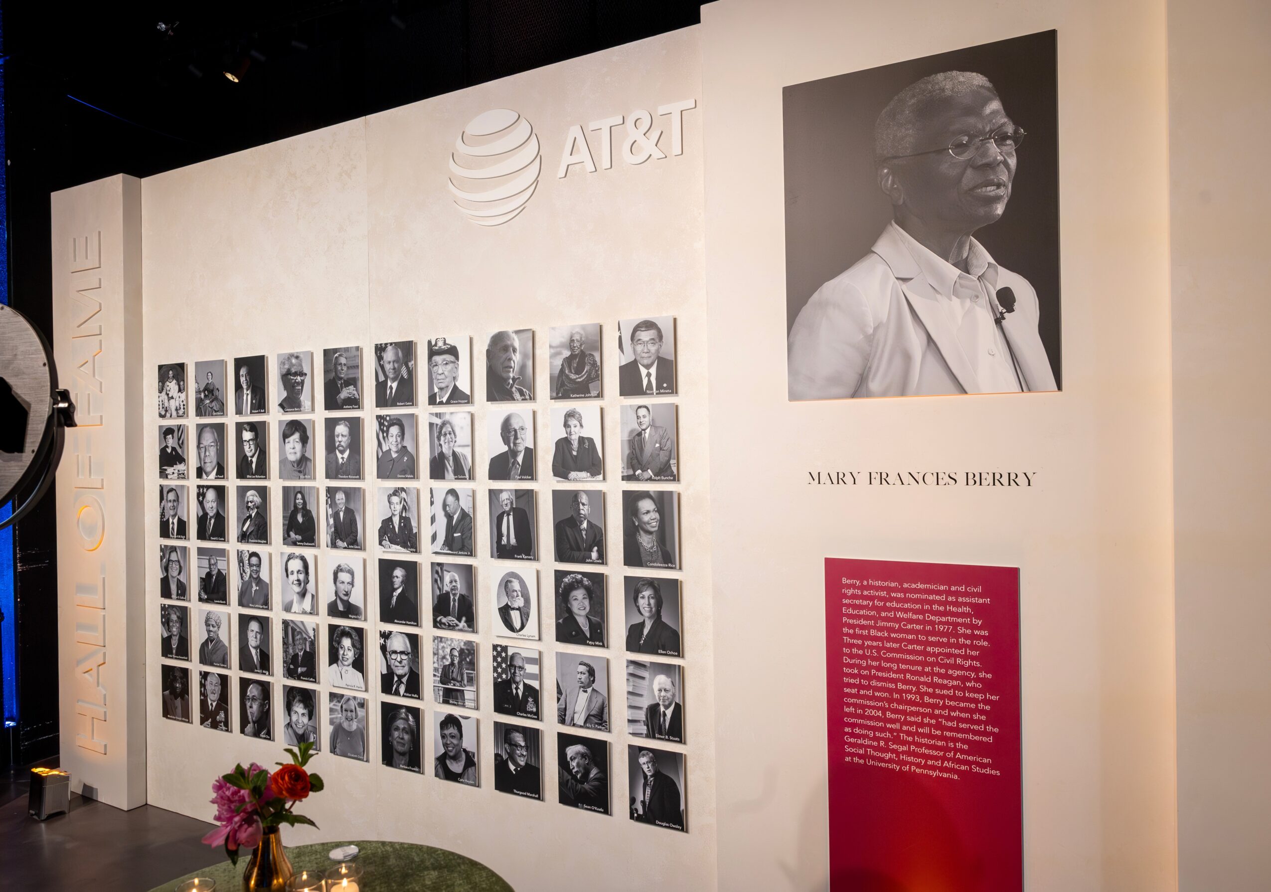 Wall display with black-and-white portraits, AT&T logo, and a large photo of a woman with glasses, along with text panel.
