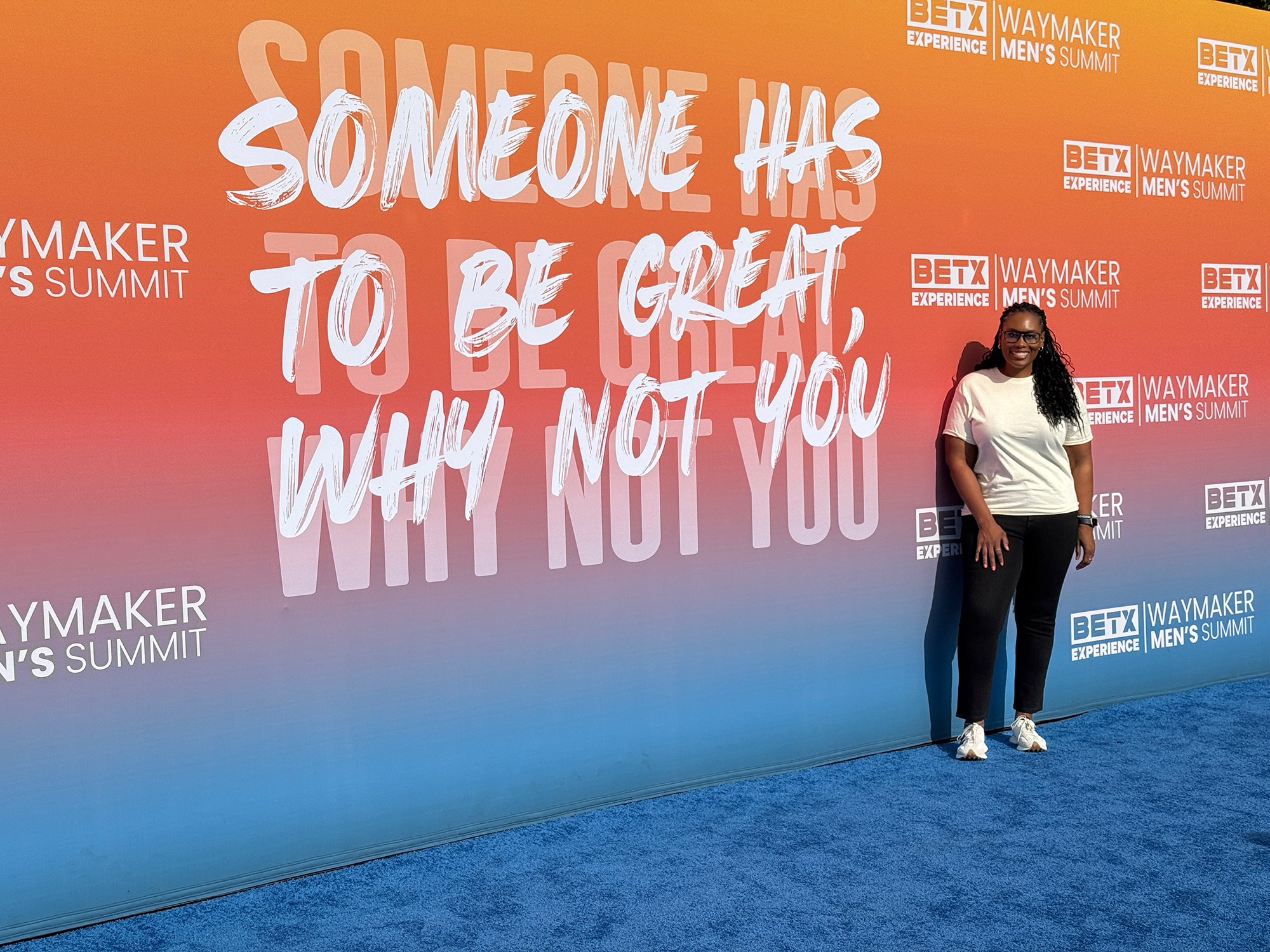 Person standing next to a large colorful wall with text about greatness and not giving up.