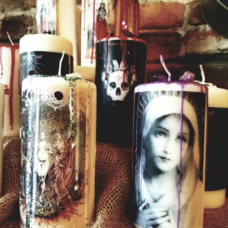 Group of candles with skull and portrait images, some with purple and white wax, displayed on a textured surface.