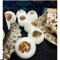 White spherical bath bombs with dried flower decorations on top, arranged on ornate silver trays.