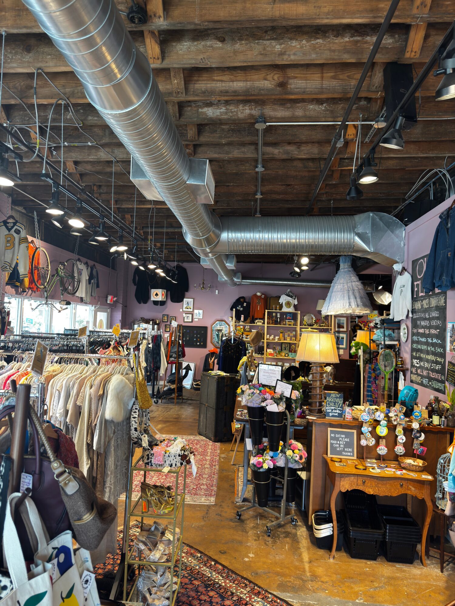 Interior of a shop with clothing, accessories, and decorative items displayed on tables and shelves, with people browsing.