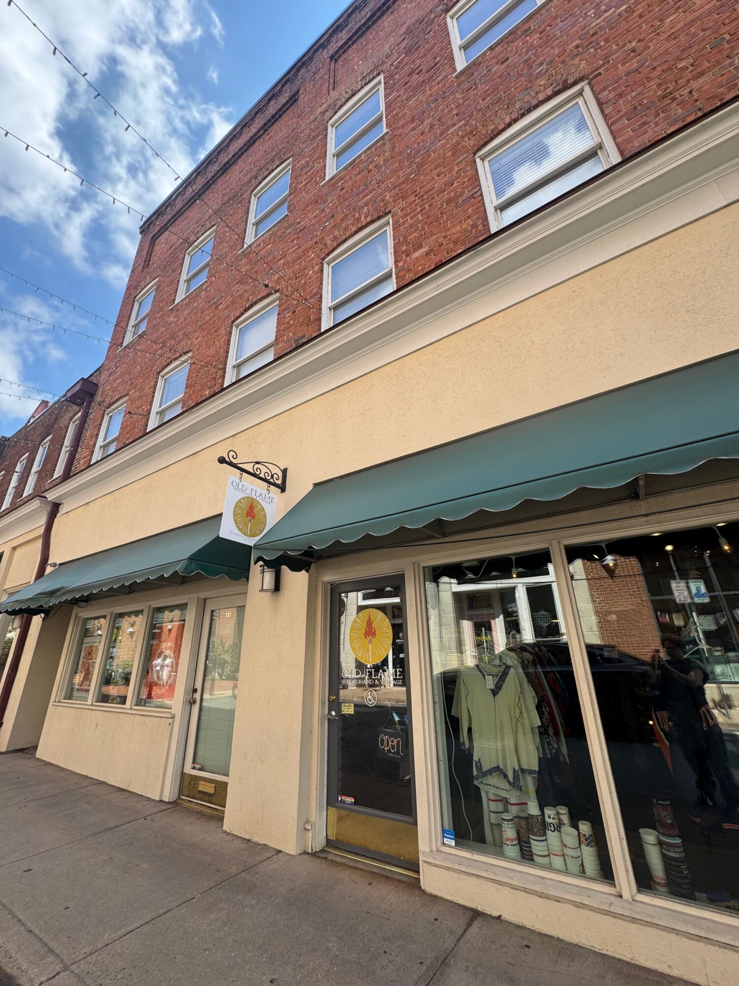 Storefront with large window, door, and awning, with a sidewalk outside and a brick building across the street.