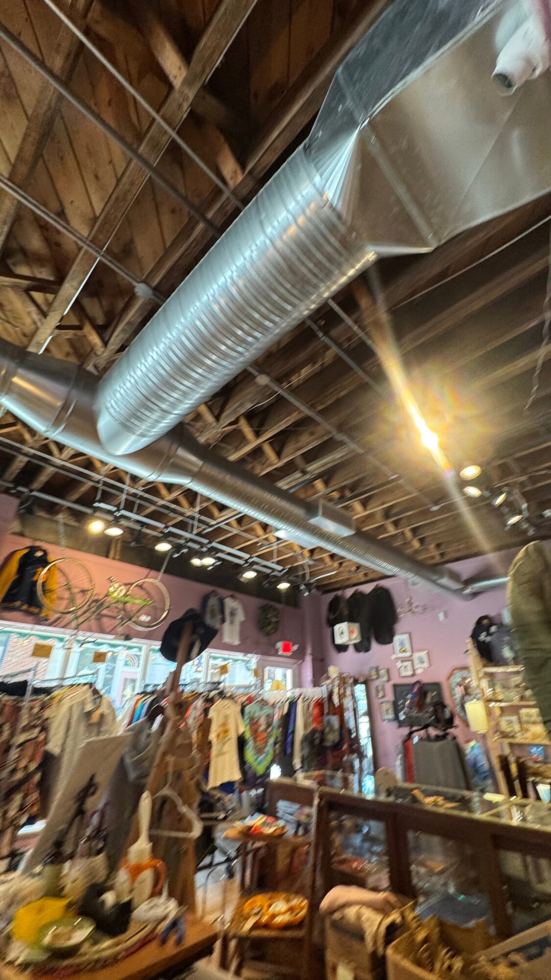 Indoor space with clothing racks, tables, and a large metal duct running along the ceiling, illuminated by warm lighting.