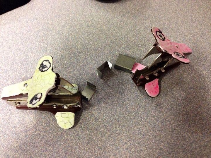 Two small paper craft animals with wings and faces on a gray surface, facing each other.