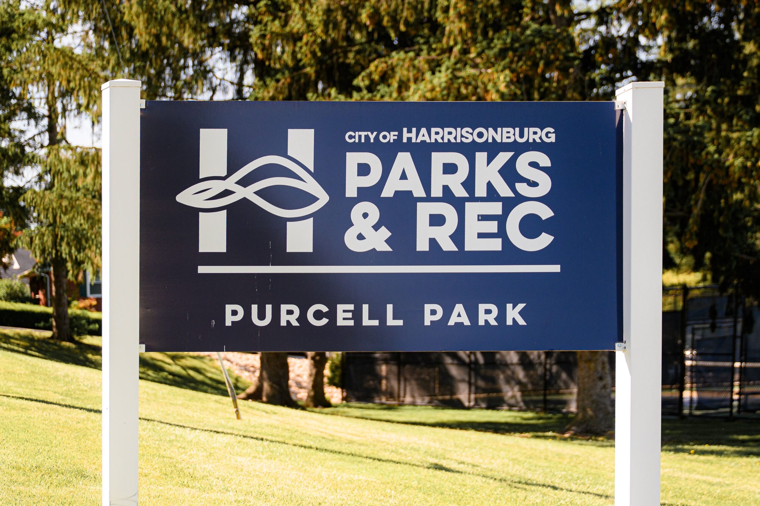 Sign for Purcell Park in Harrisonburg, with trees and grass in the background.