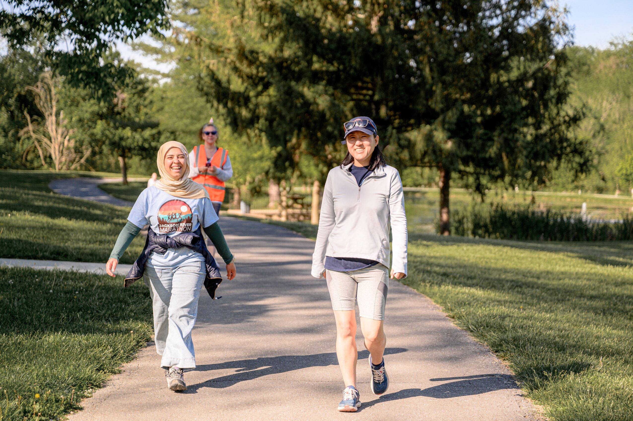 Three people walking on a park path with trees and grass in the background, two women in front and a man behind.