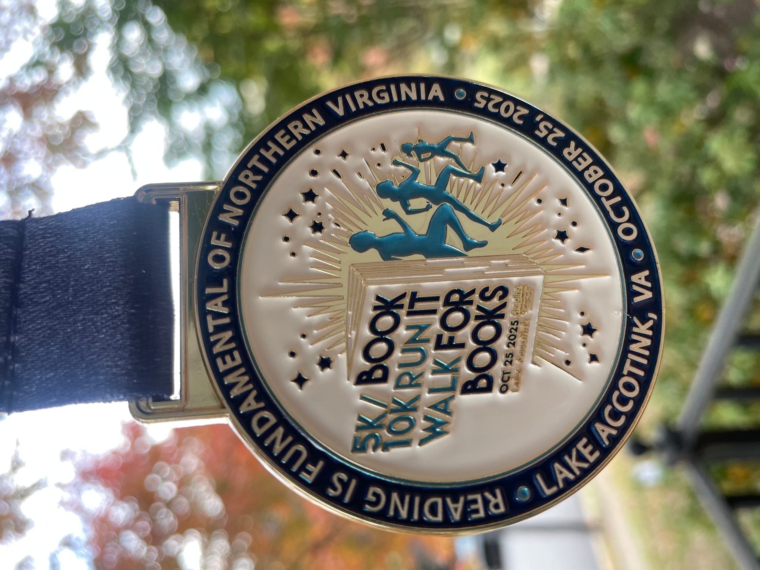Clock face with a blue and white logo, trees in the background, and a black strap on the left side.