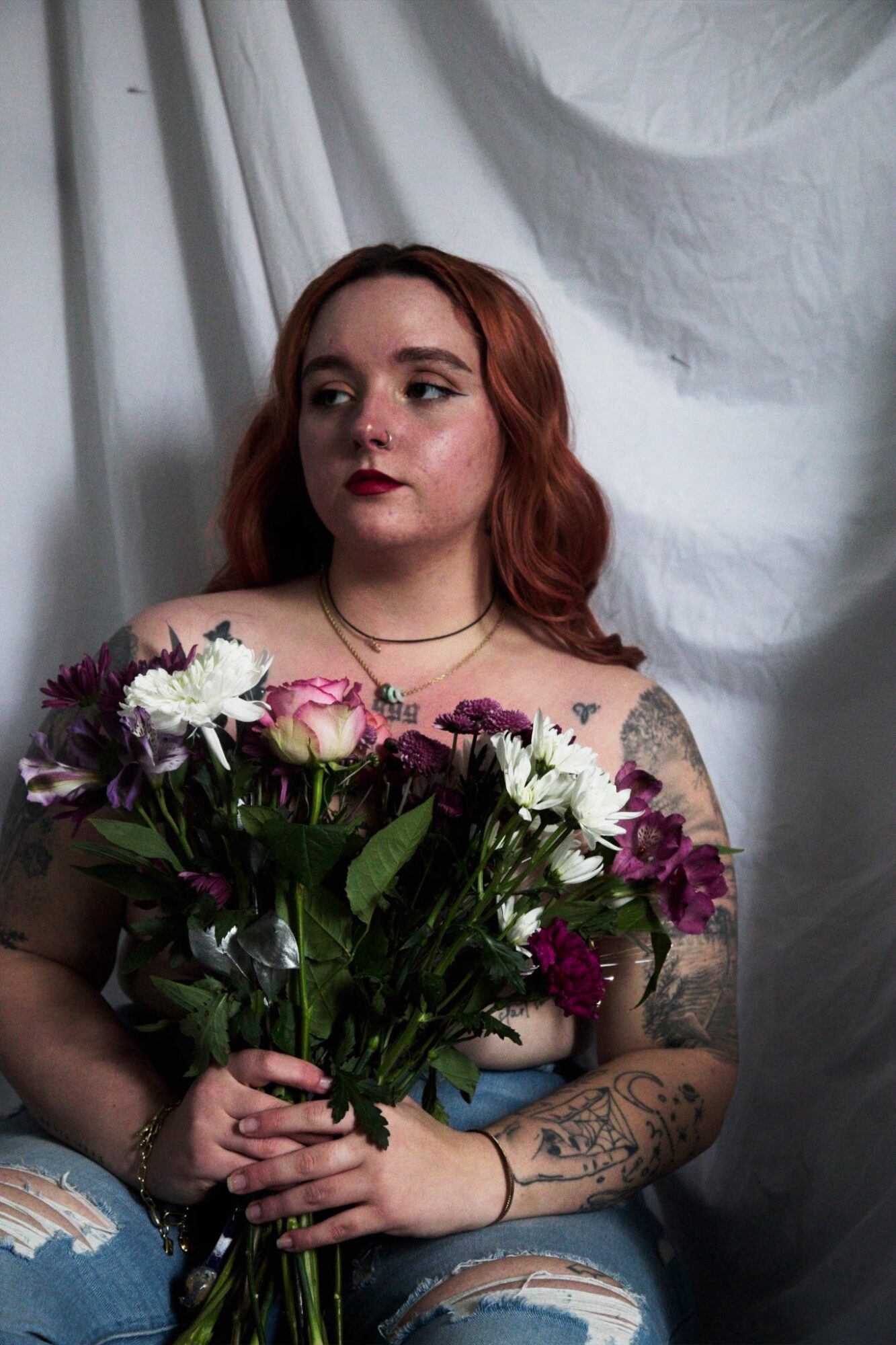 Young woman with red hair holding a bouquet of flowers, sitting against a white fabric backdrop.