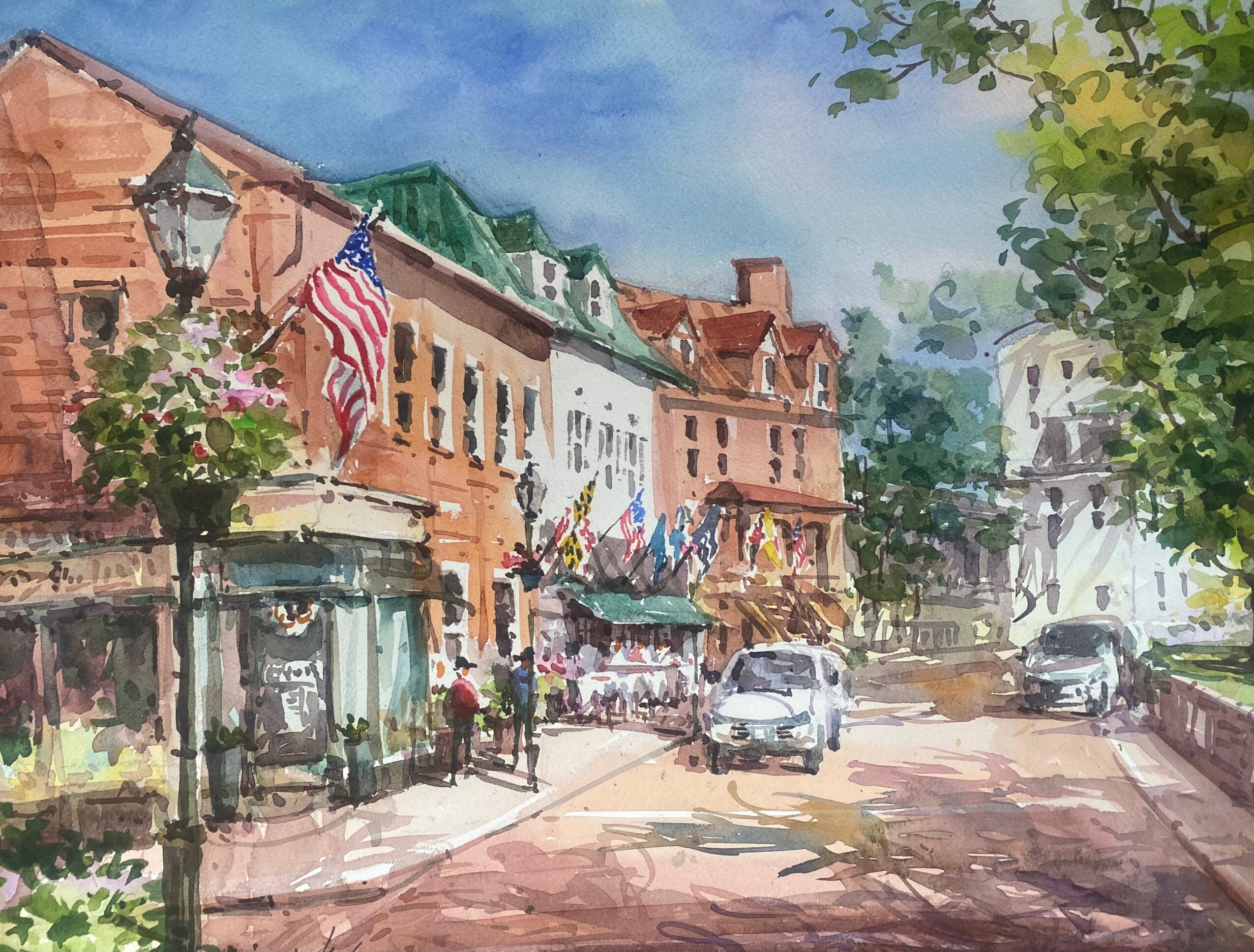 Street scene with buildings, flags, trees, cars, and pedestrians under a blue sky.