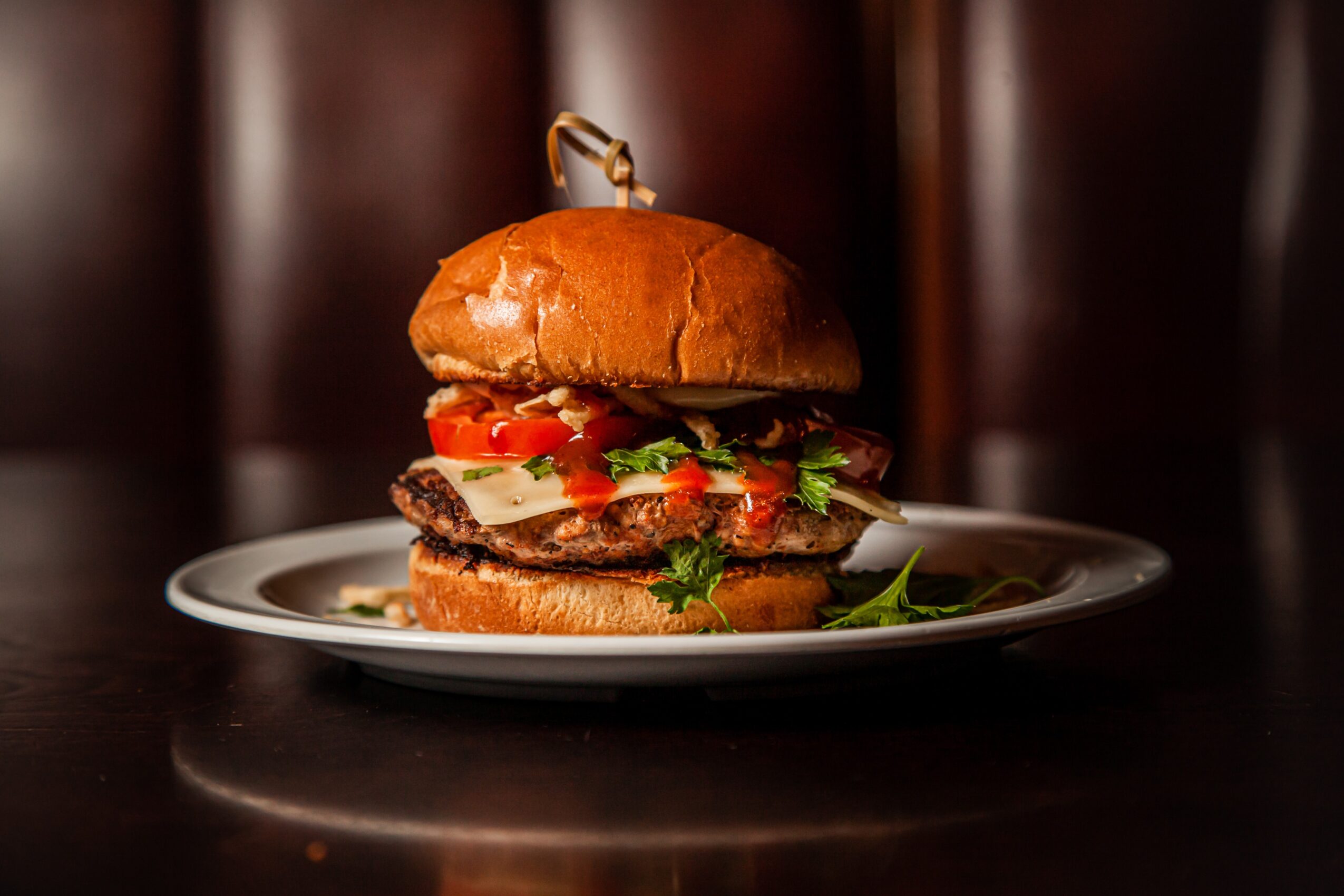 Hamburger with lettuce, tomato, and cheese on a plate, with a dark background.