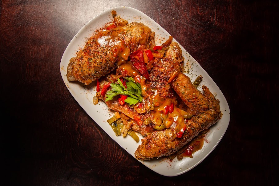 Fried chicken pieces with vegetables and sauce on a white oval plate, dark wooden background.