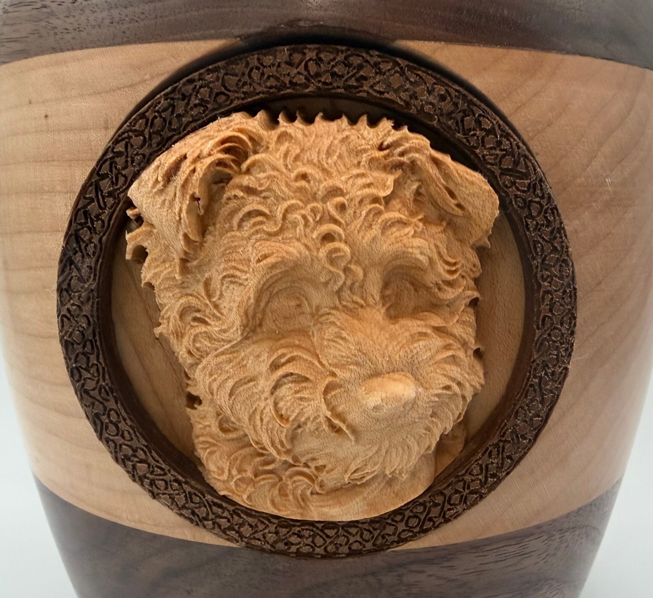 Wooden sculpture of a dog's face inside a circular frame, detailed fur texture, mounted on a wooden surface.