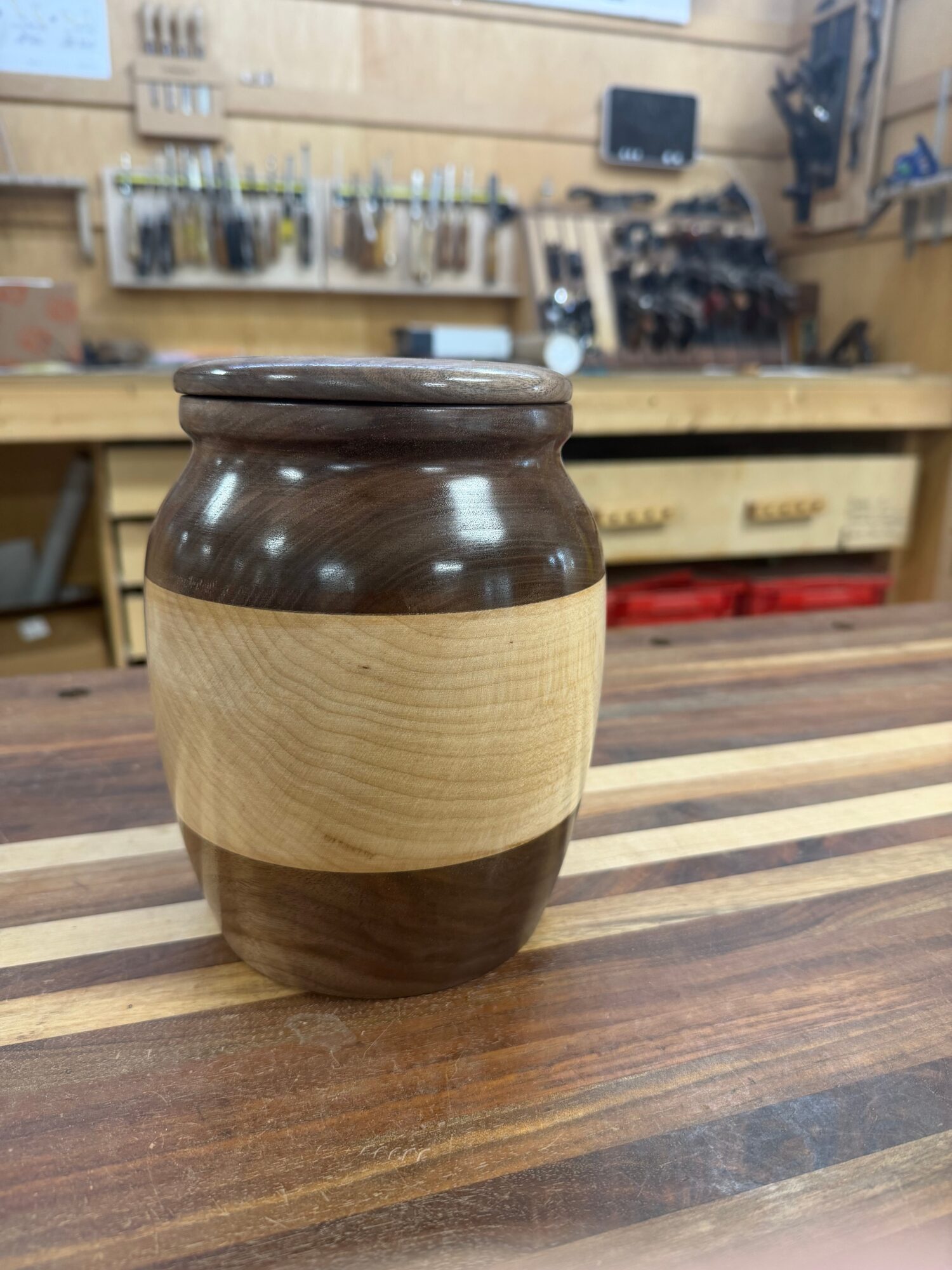 Wooden and dark brown ceramic vase on a striped wooden table in a workshop setting.