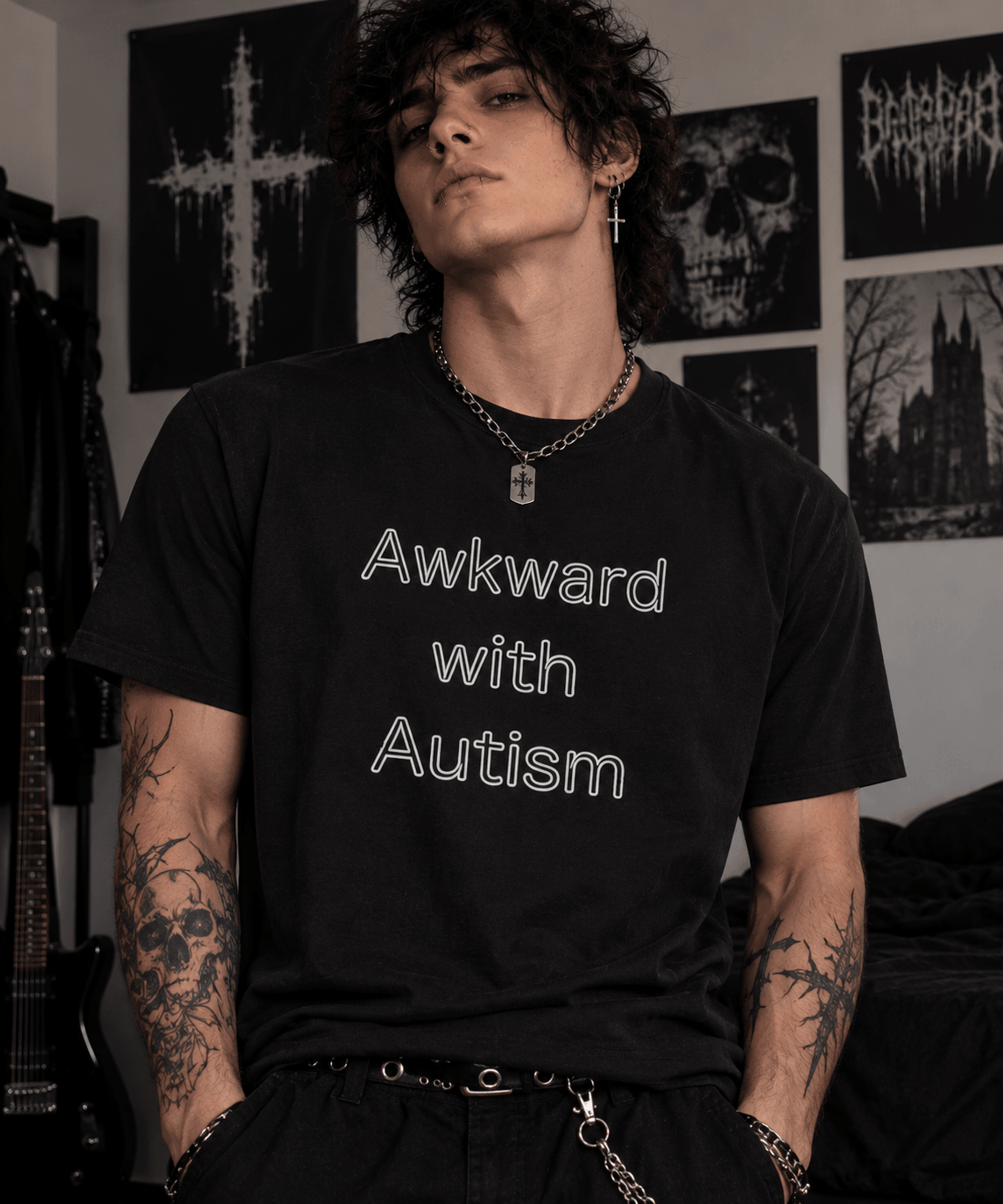 Young person with curly hair wearing a black T-shirt with white text, standing in a room with dark artwork on the wall.