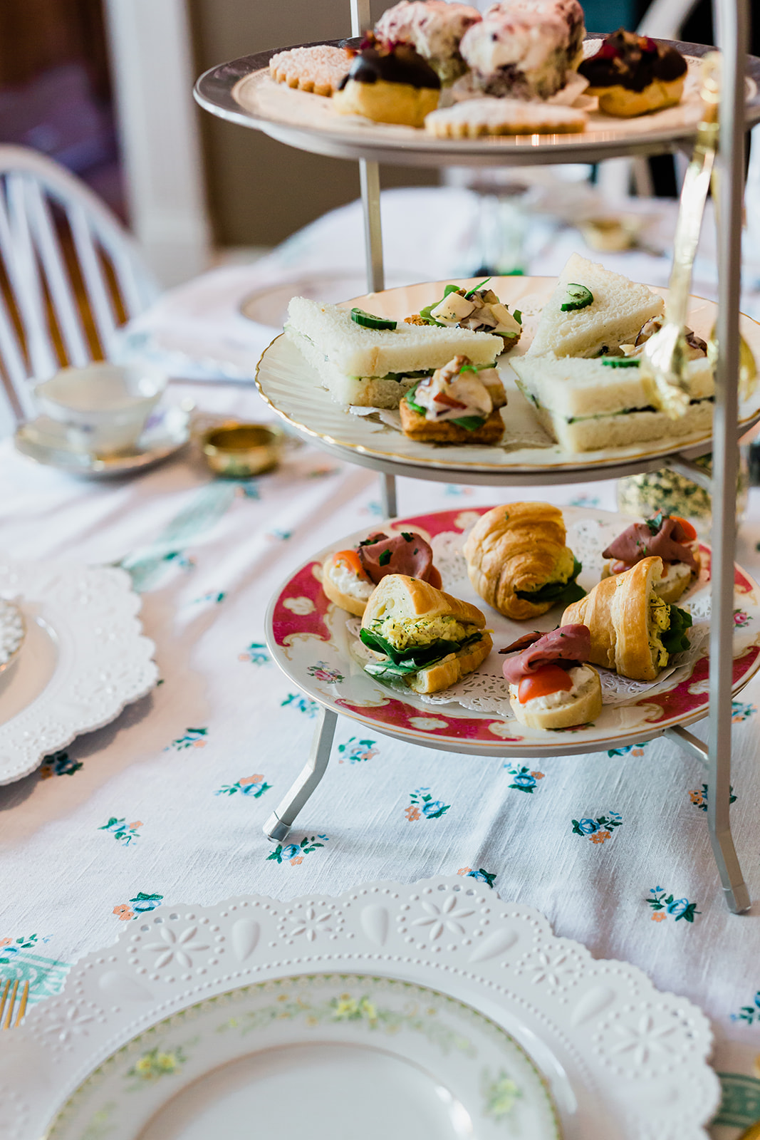 Three-tiered serving stand with assorted pastries and sandwiches on a table with a white lace tablecloth.