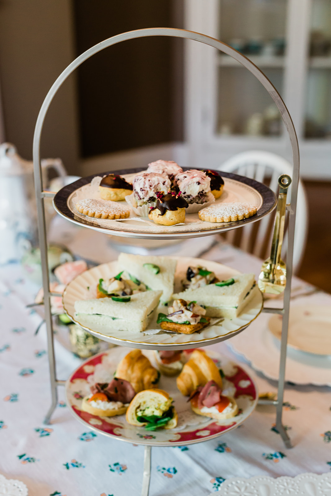 Three-tiered dessert stand with assorted pastries and sweets, set on a table with a floral tablecloth.