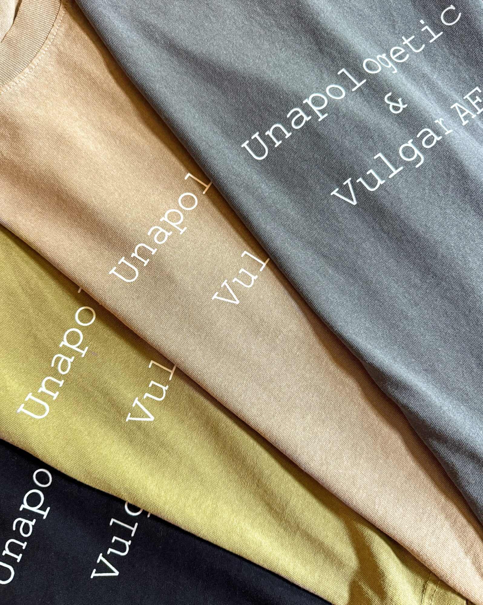 Three folded fabric pieces in beige, gray, and yellow with white text printed on them, arranged diagonally.
