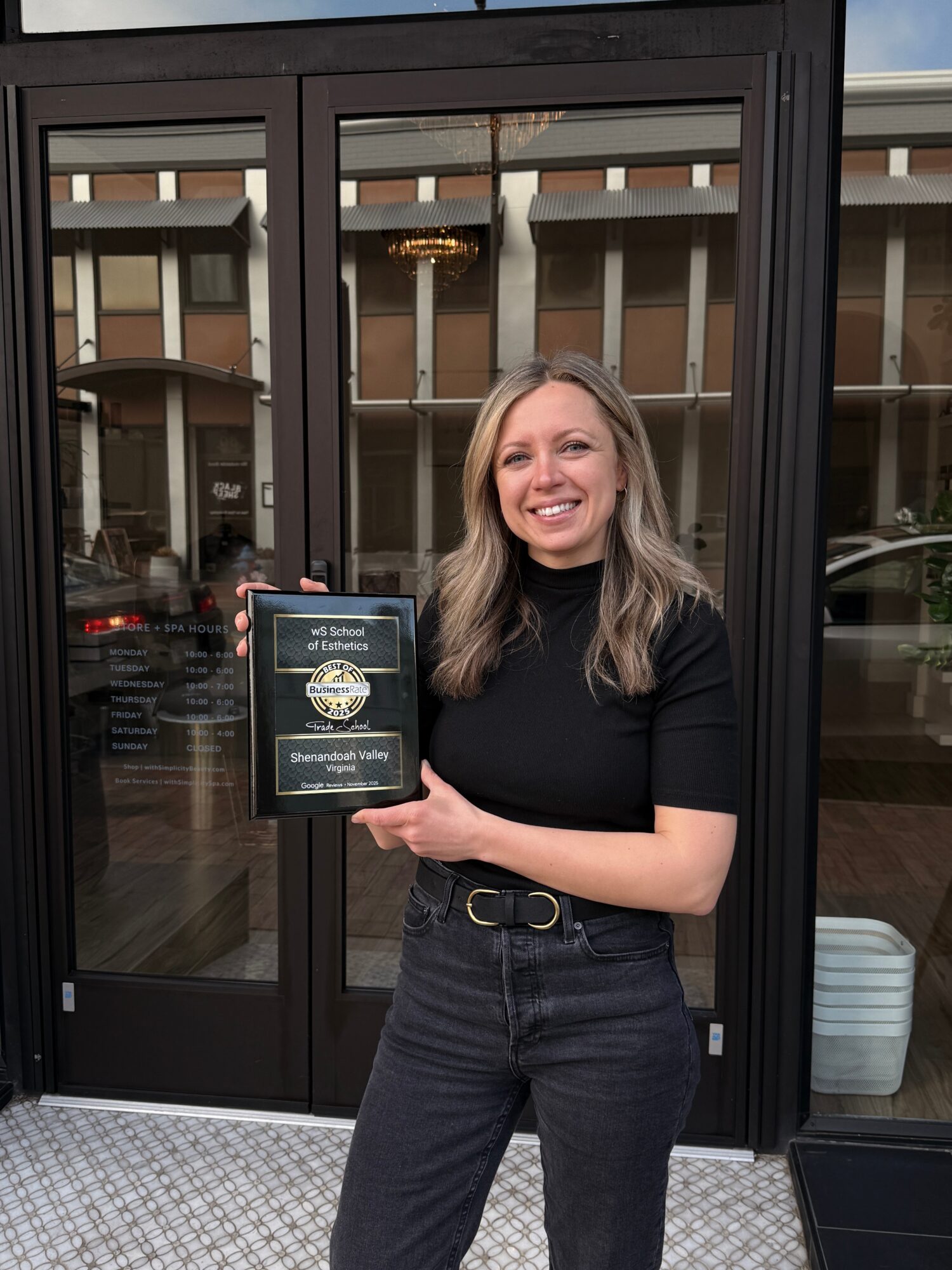 Woman with long hair smiling and holding a plaque in front of glass doors.