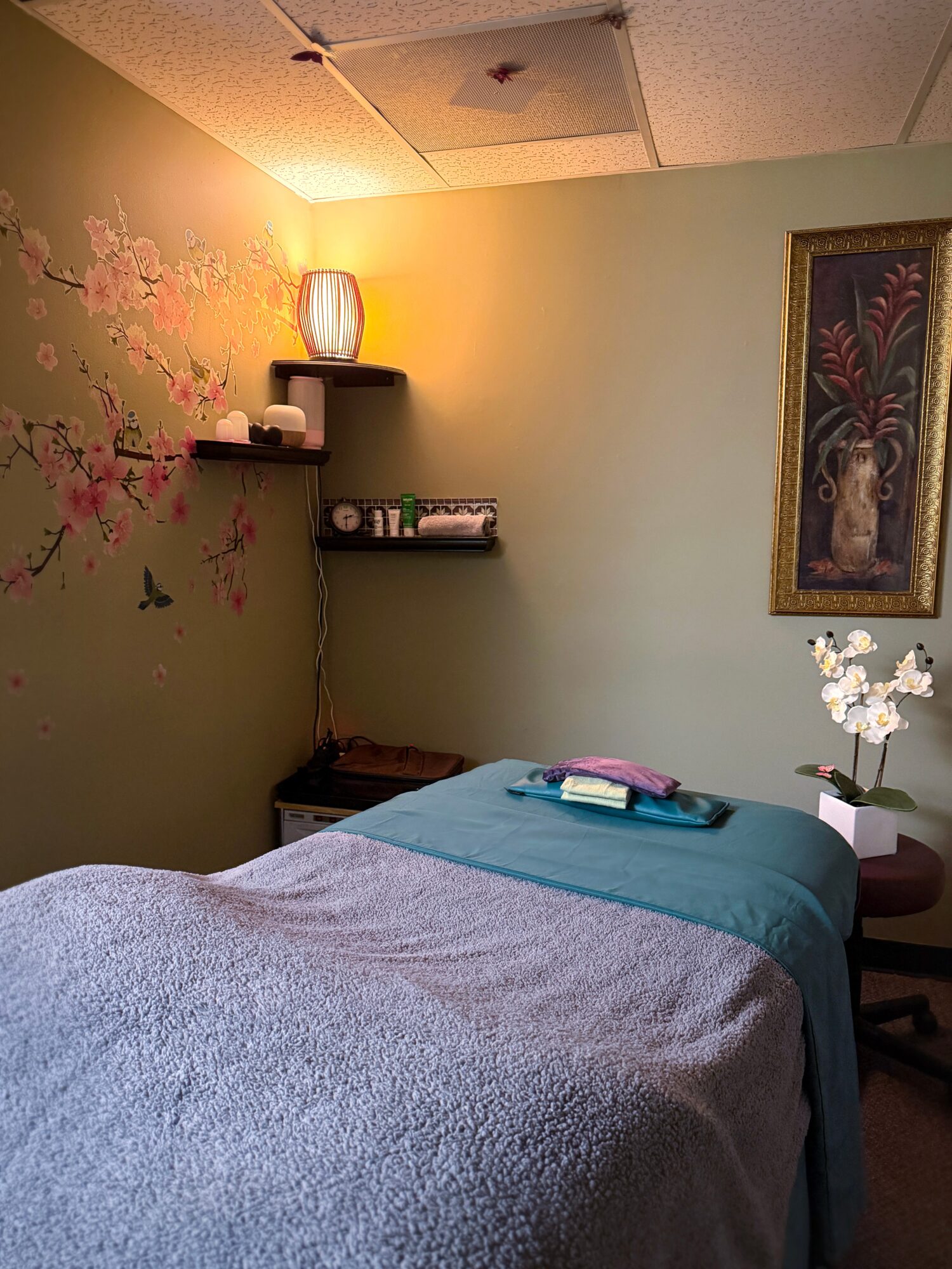 A bedroom with a bed, wall art, shelves, a lamp, and a flower arrangement on a nightstand.