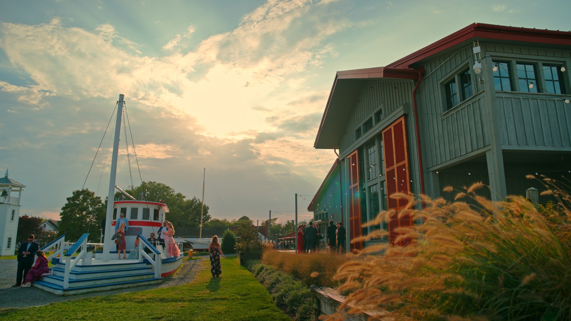 People near boats and a building with a sunset sky in the background.