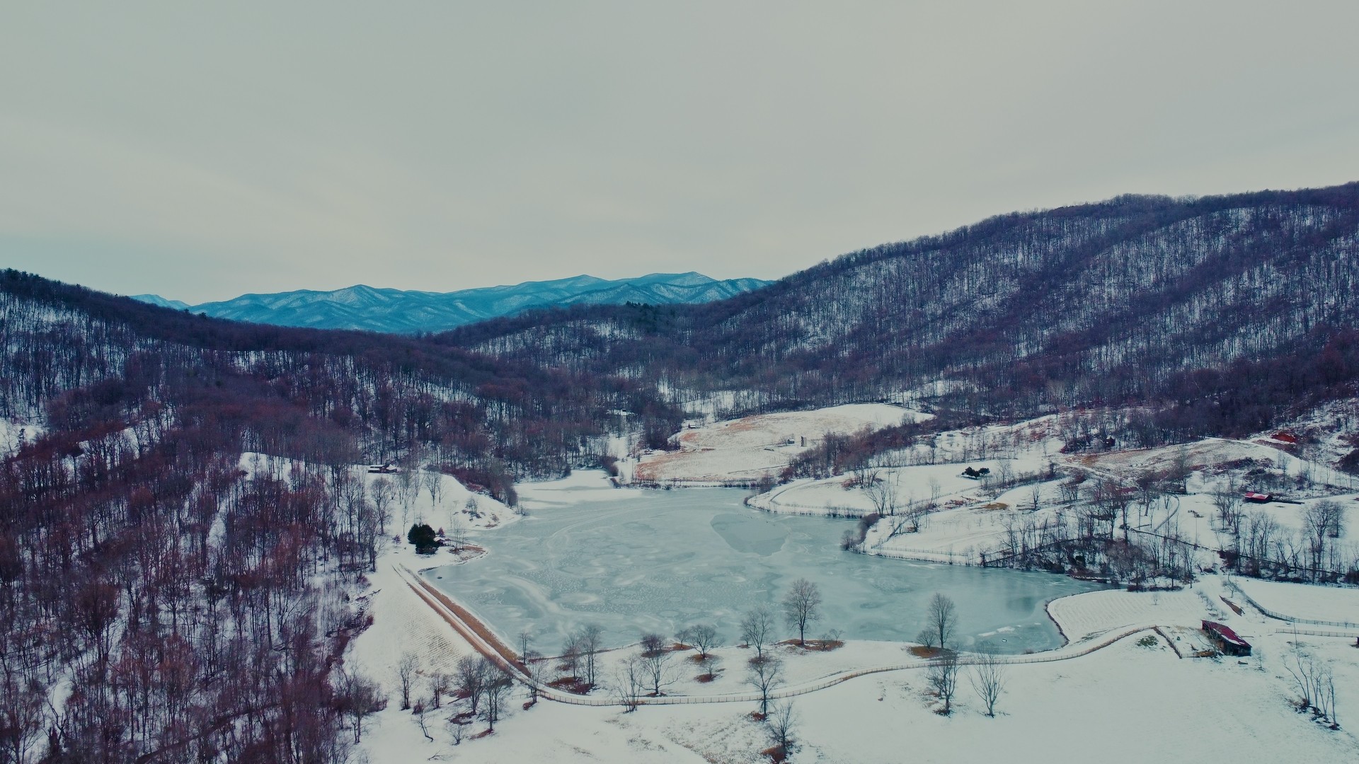 Snow-covered landscape with hills, a river, and trees, under a cloudy sky.